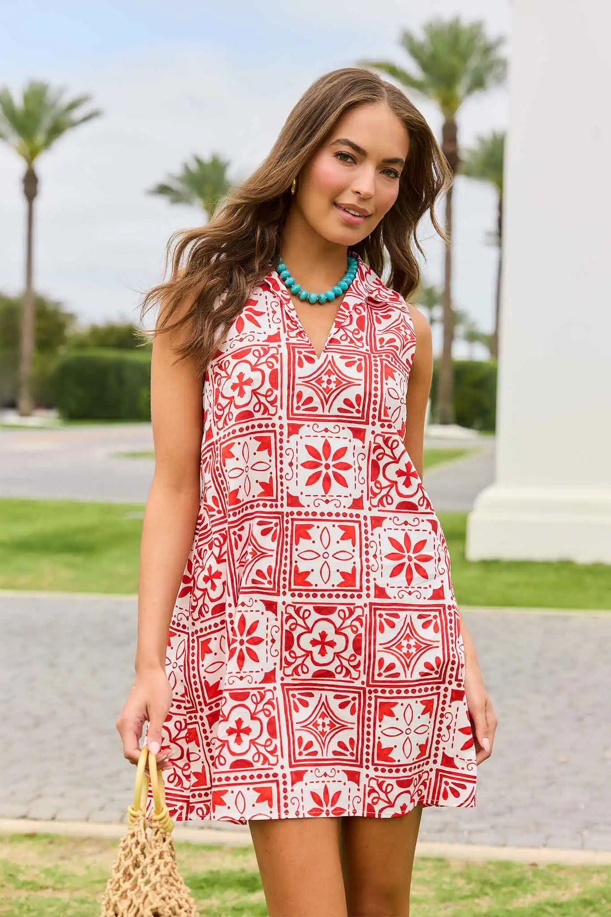 Woman wearing a red and white patterned dress standing outdoors with palm trees in the background