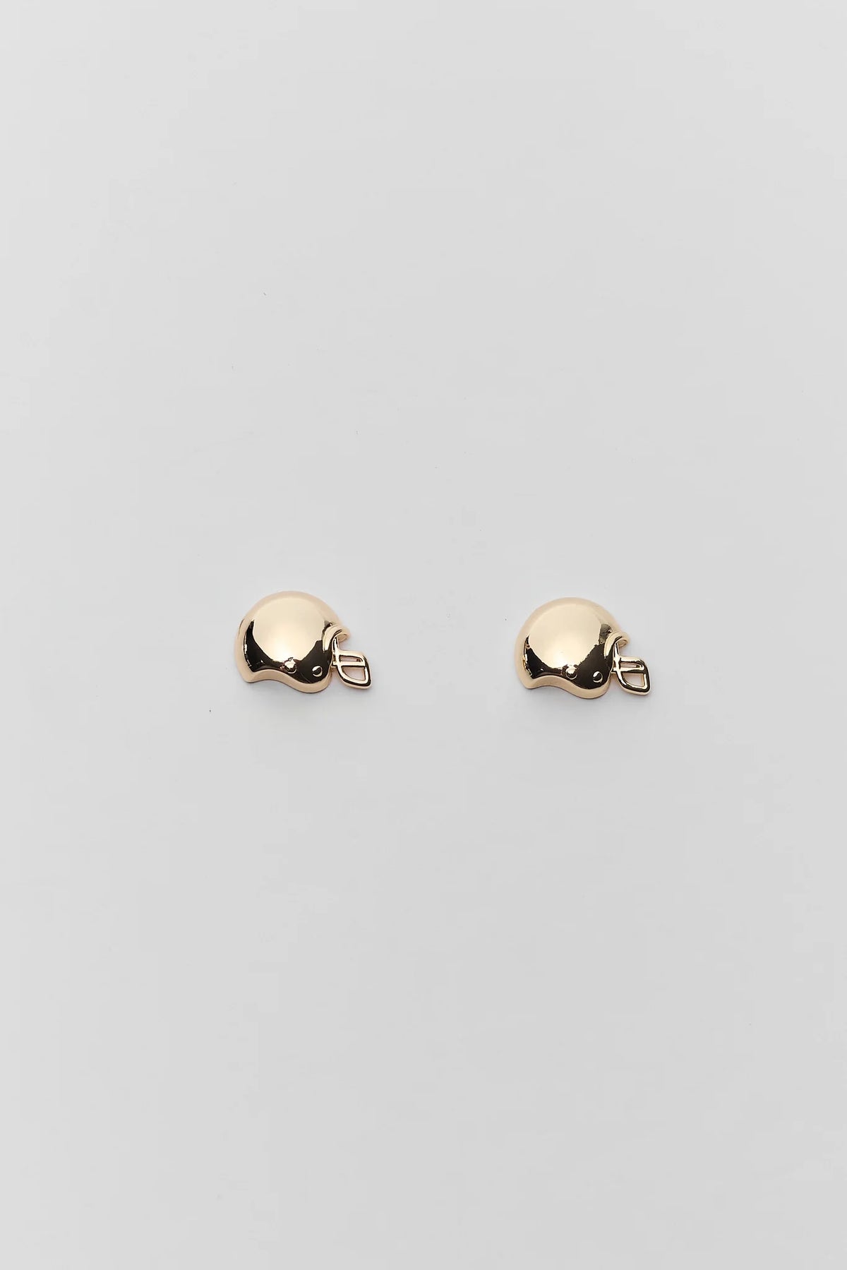 Pair of gold football helmet stud earrings, flat lay on light gray background | Avara