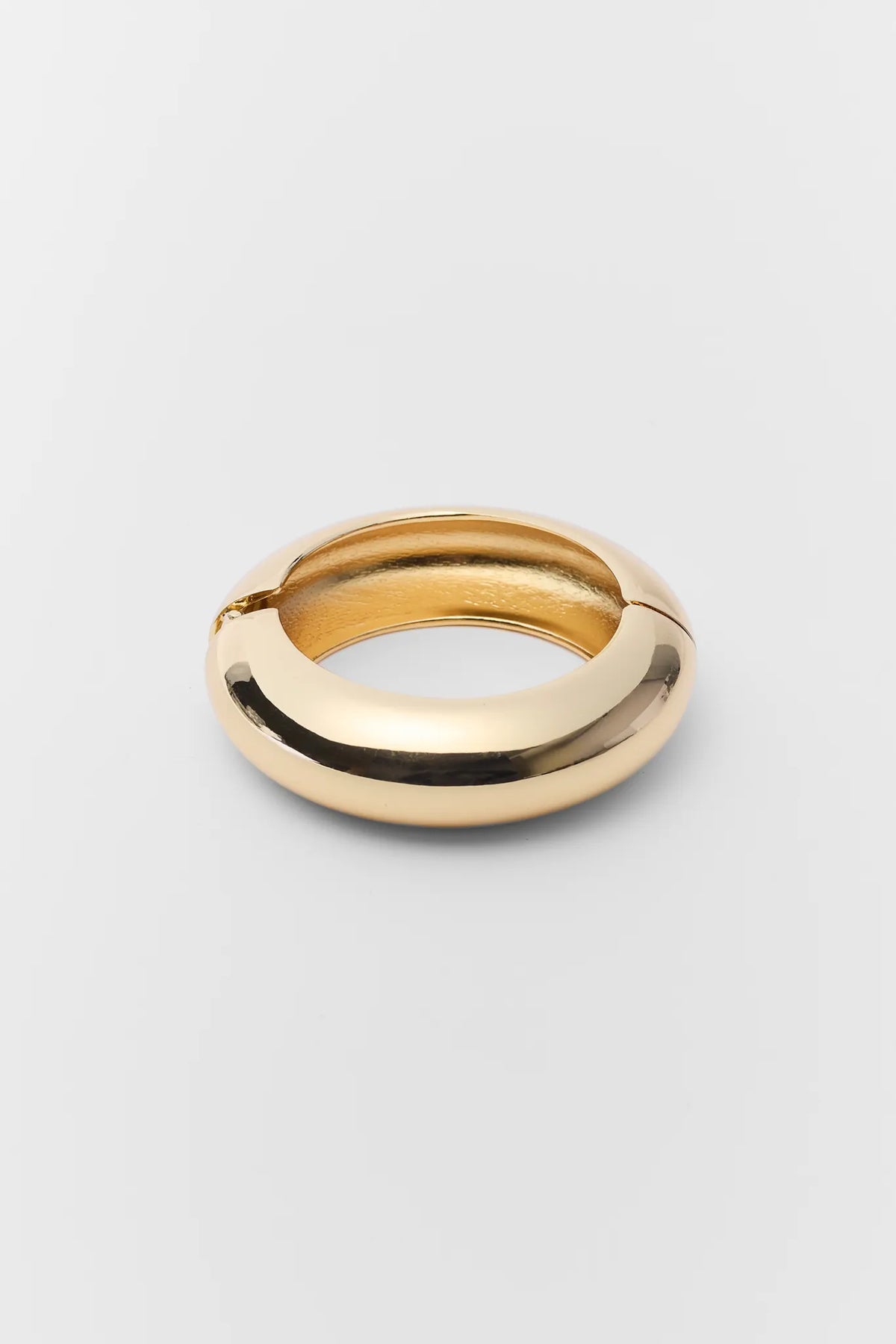 Marisol Gold Bangle Bracelet with a chunky design, polished finish, and hinge closure, set against a simple background, highlighting its chic and versatile style.