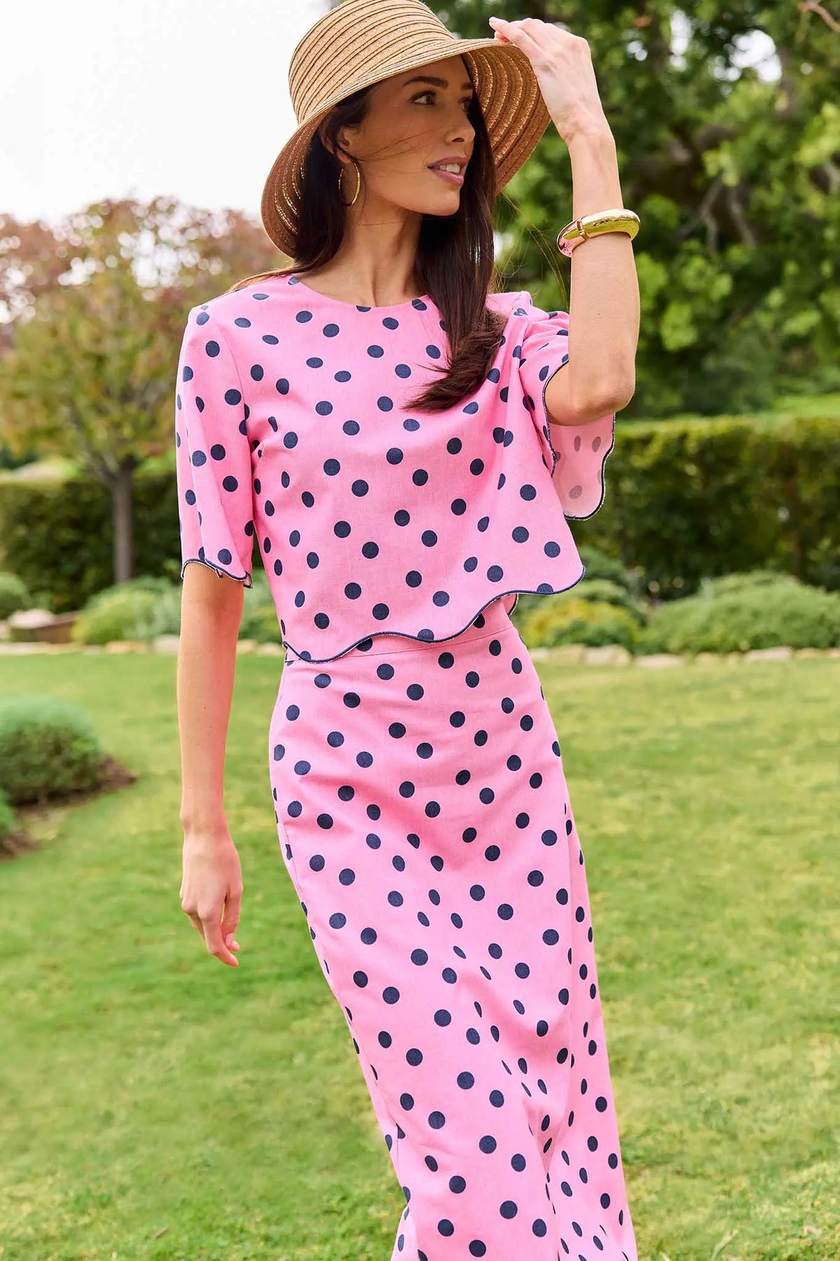 Pink polka dot top with navy dots, scalloped hem, styled with matching skirt and straw hat outdoors | Avara