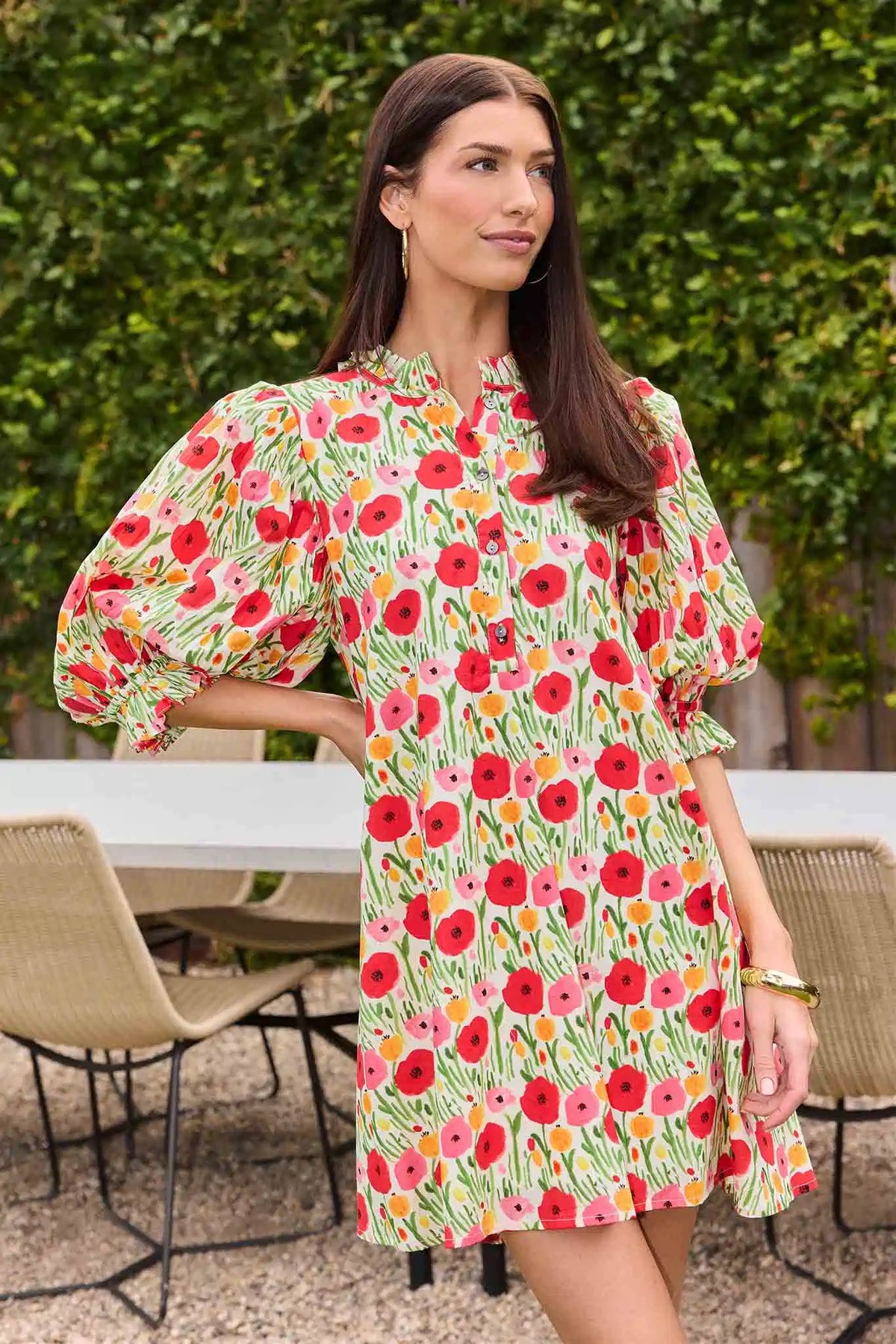 Woman wearing a floral dress standing outdoors with greenery in the background
