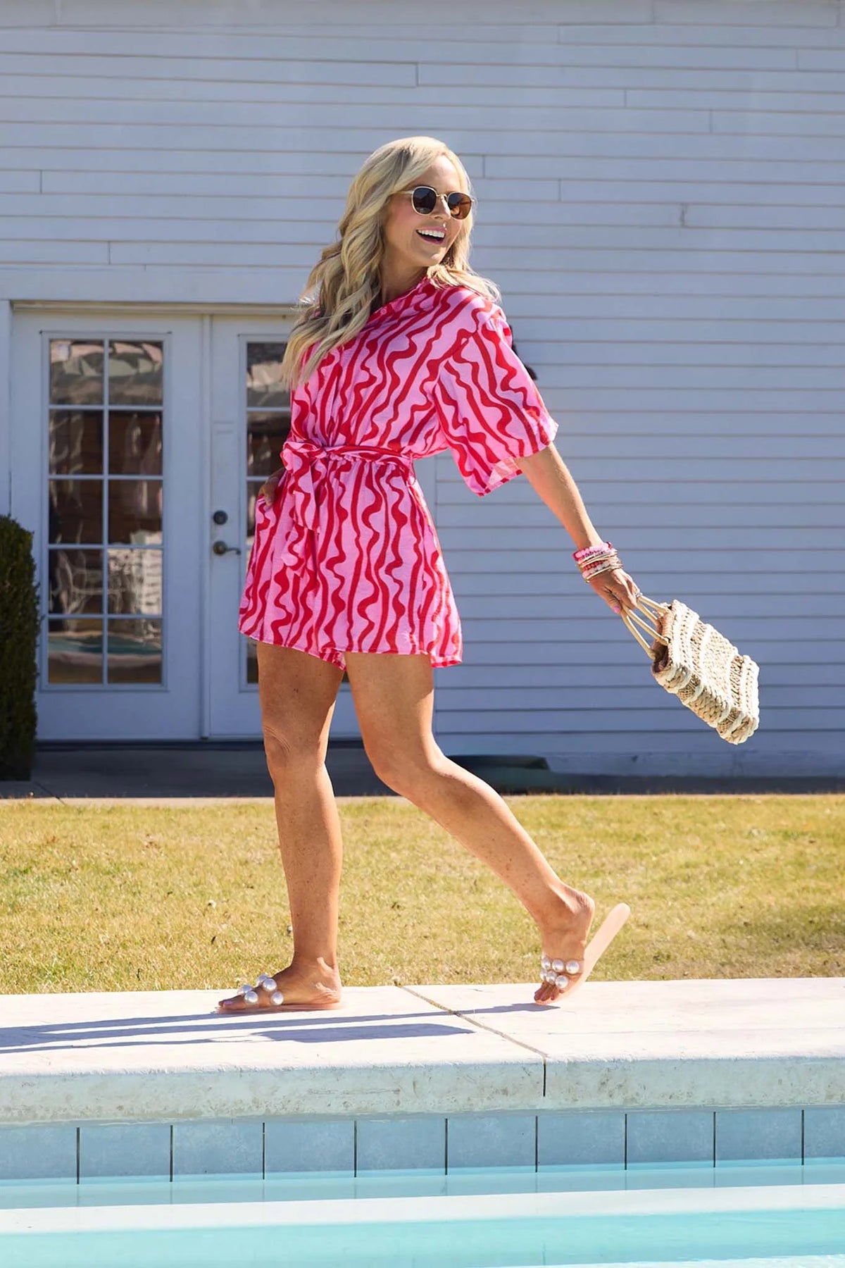 Woman in a pink and white patterned dress standing by a pool.