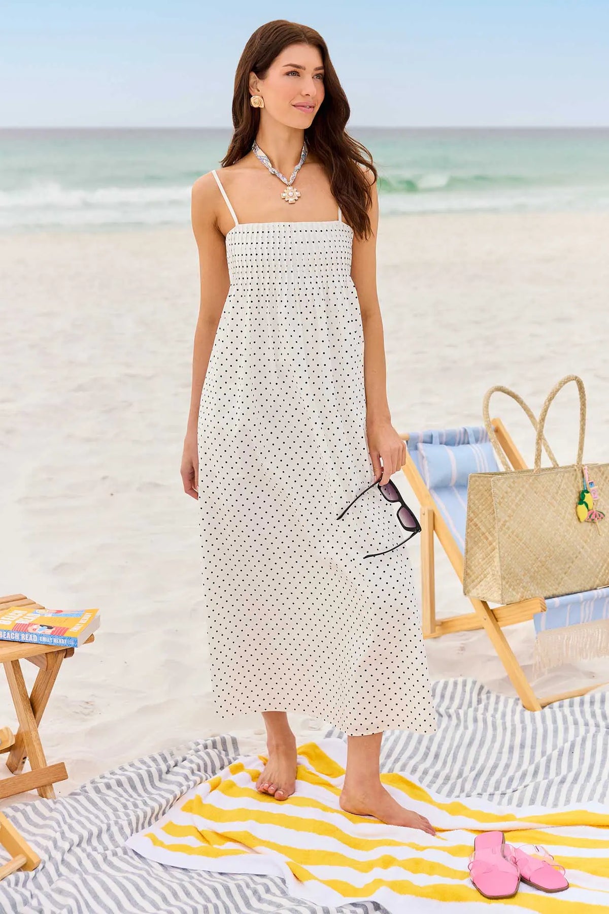 Woman in a white dress on a beach with a yellow towel and pink shoes.
