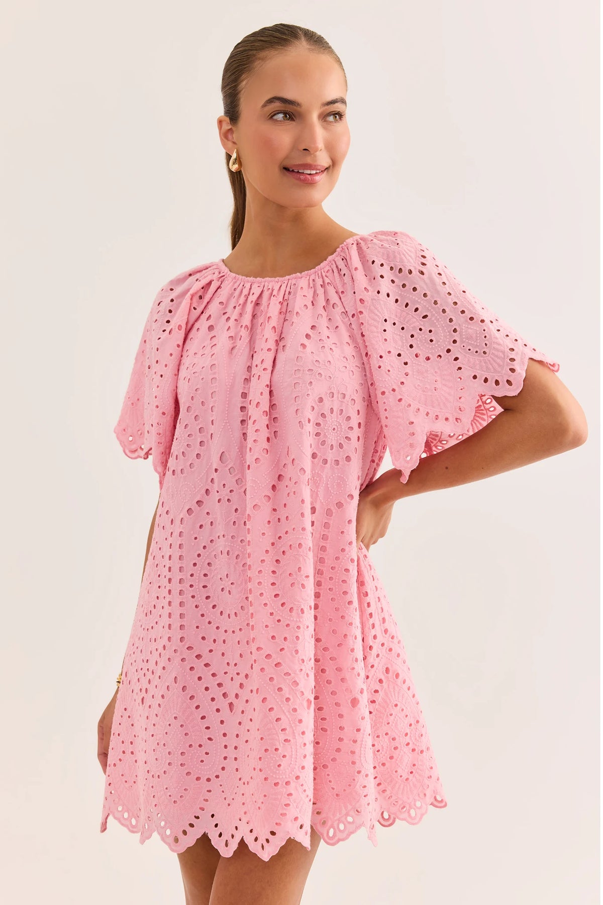 Woman wearing pink eyelet tunic dress, 3/4 view showing scalloped hem and flutter sleeves | Avara