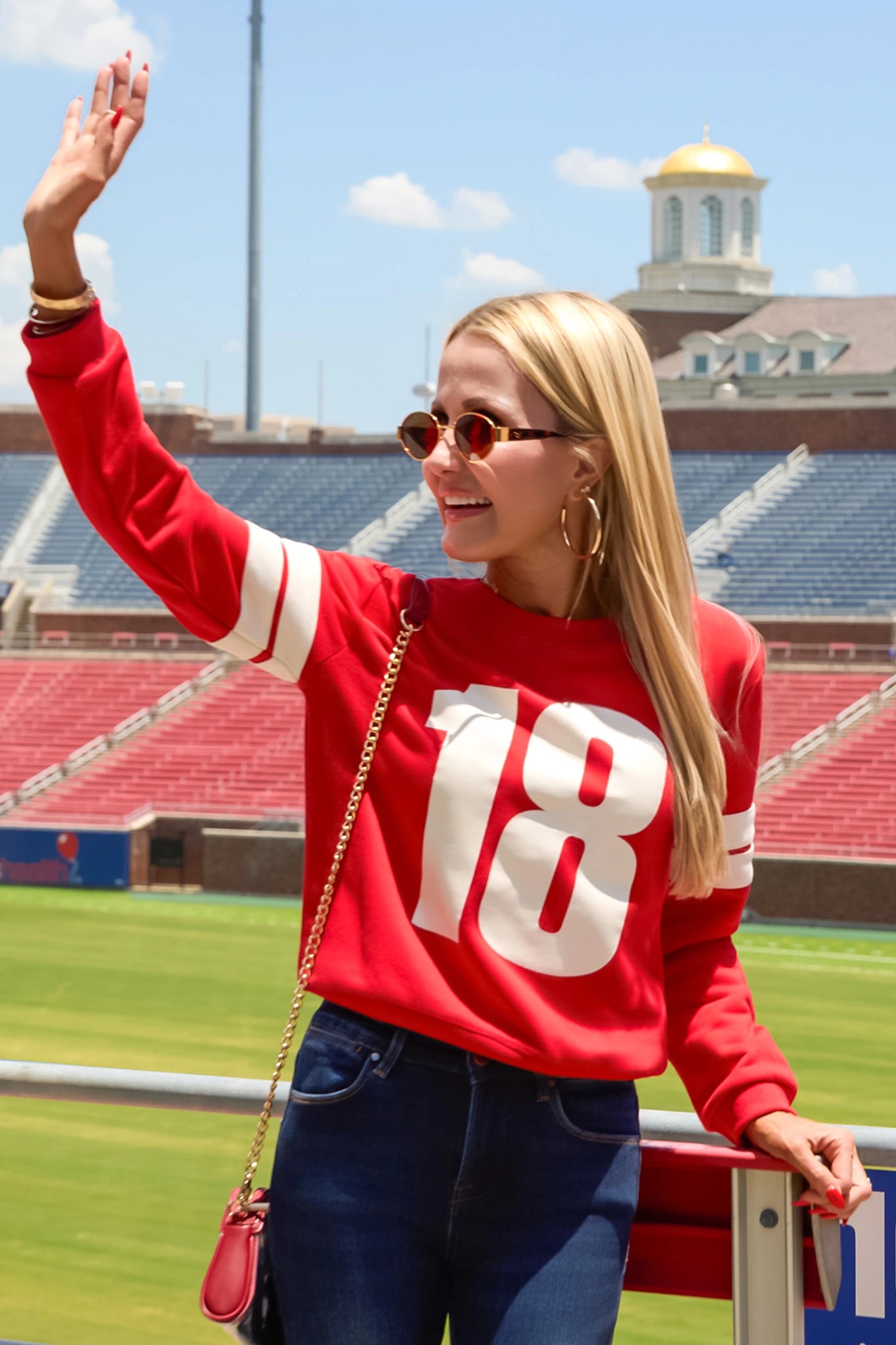 Red Varsity Number 18 Pullover styled for game day at a stadium with jeans and red crossbody bag | Avara