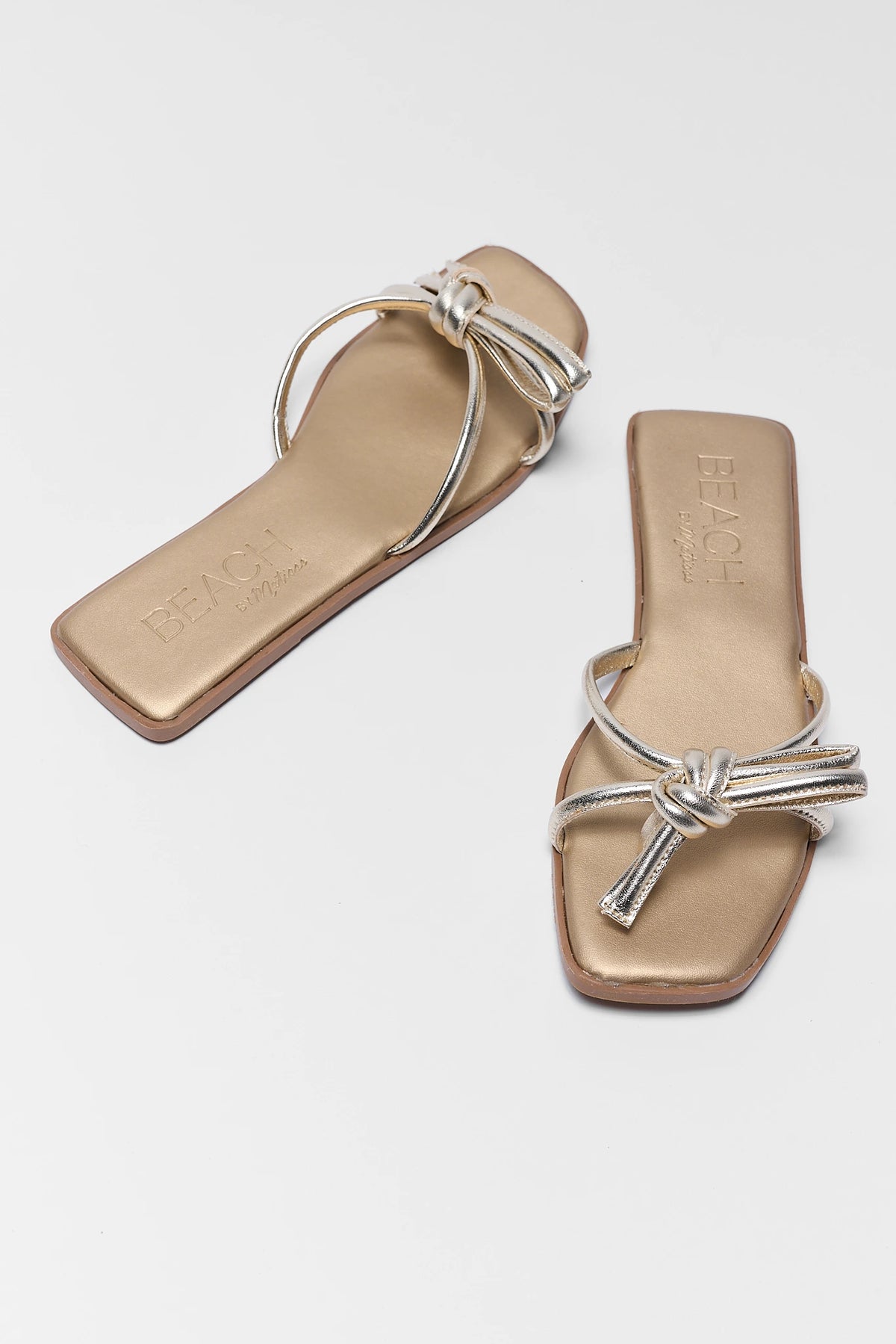 Pair of gold metallic knot sandals flat lay angled view - Ruthie by Matisse | Avara