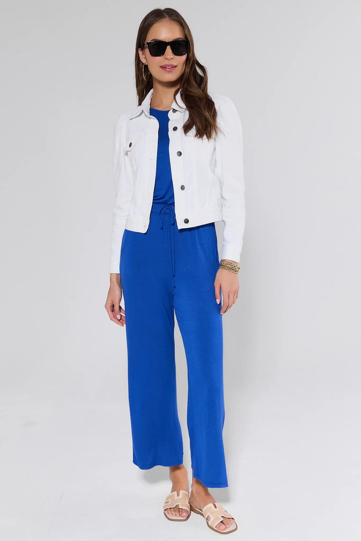 Roxanna White Denim Jacket full-length styled look with blue jumpsuit, sunglasses, and slide sandals | Avara
