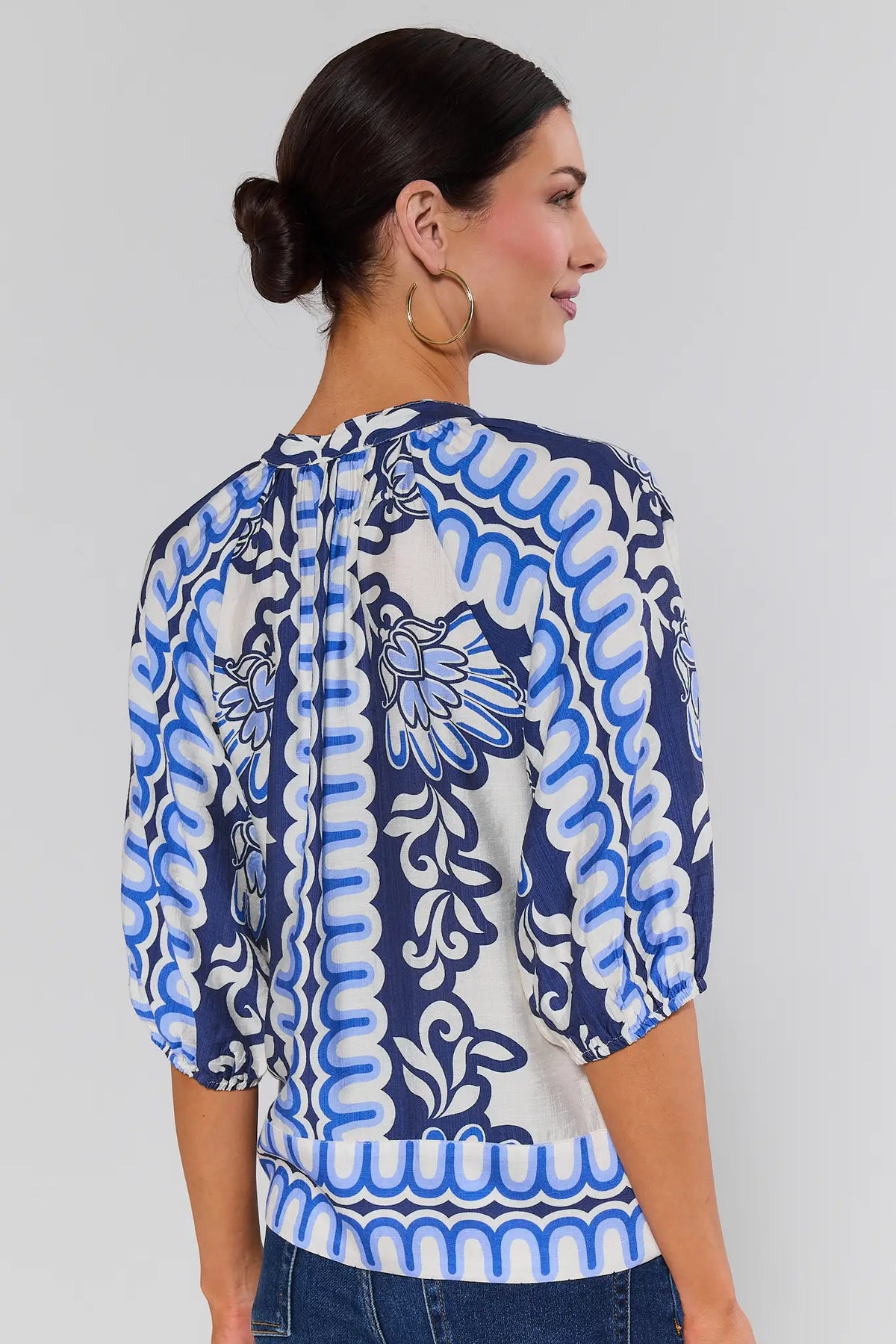 Woman standing wearing a blue and white patterned blouse against a gray background