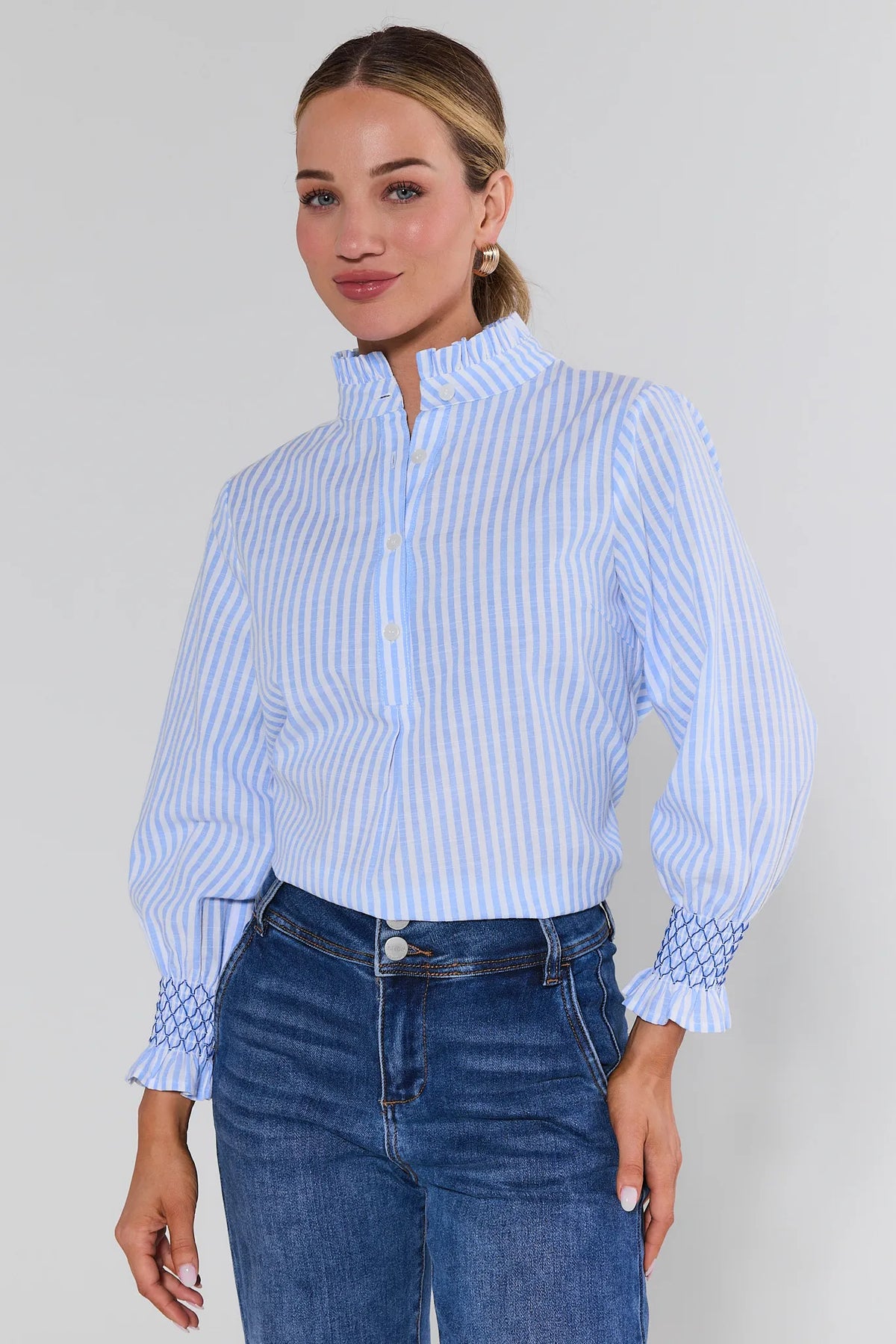 Woman wearing a blue and white striped shirt and jeans against a plain background