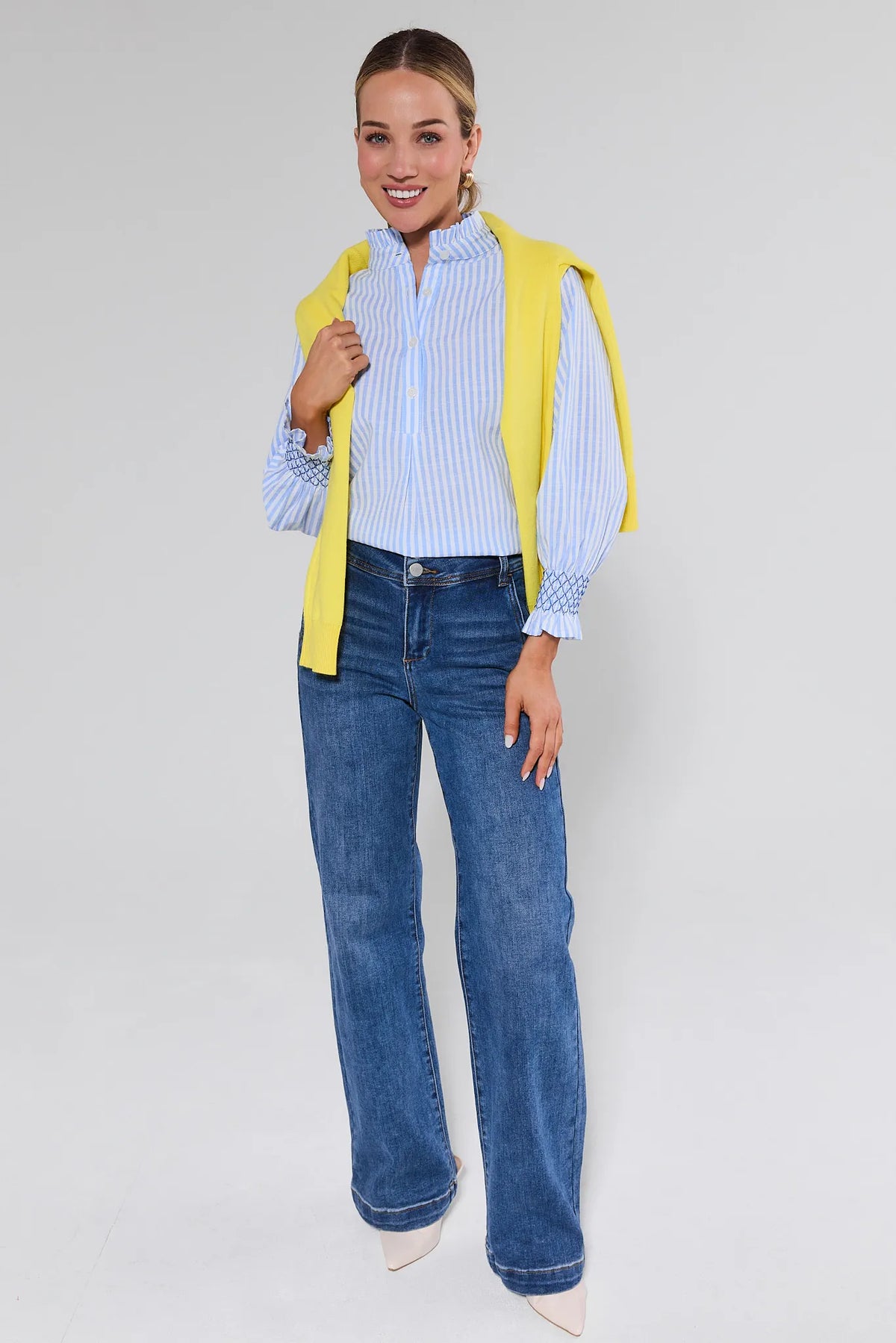 Woman wearing a yellow cardigan, blue jeans, and a striped shirt on a white background