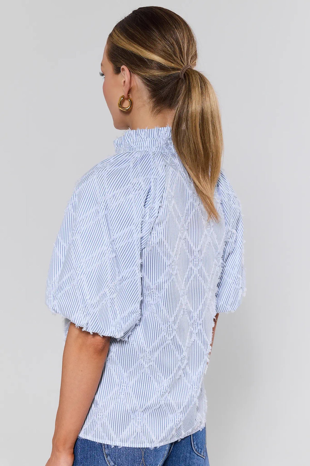 Woman standing wearing a light blue and white striped shirt with a background