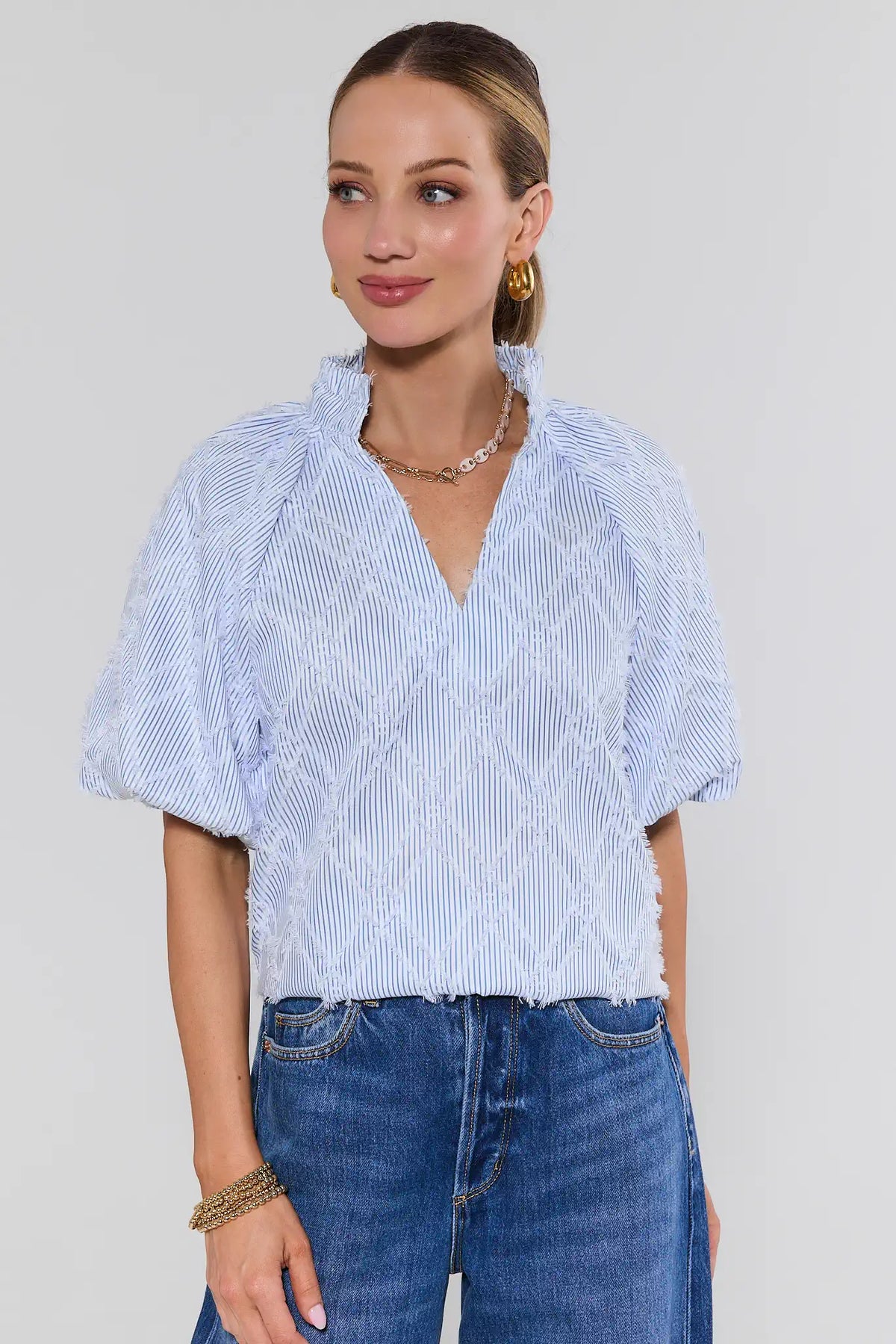 Woman wearing a blue and white patterned blouse and blue jeans against a plain background