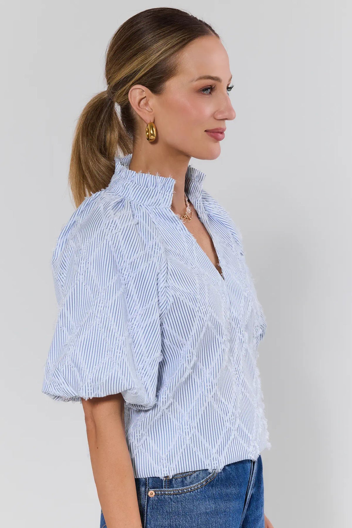 Woman wearing a blue and white striped shirt with denim pants on a plain background