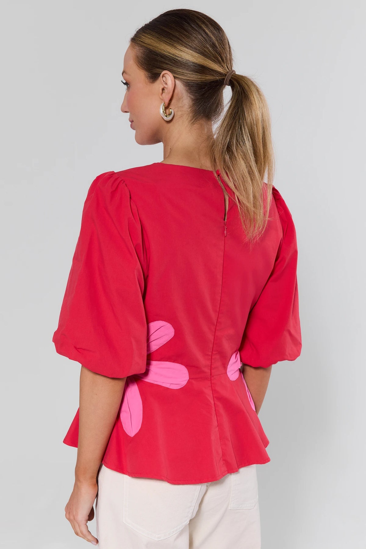 Woman wearing a red blouse with pink floral patterns on a plain background