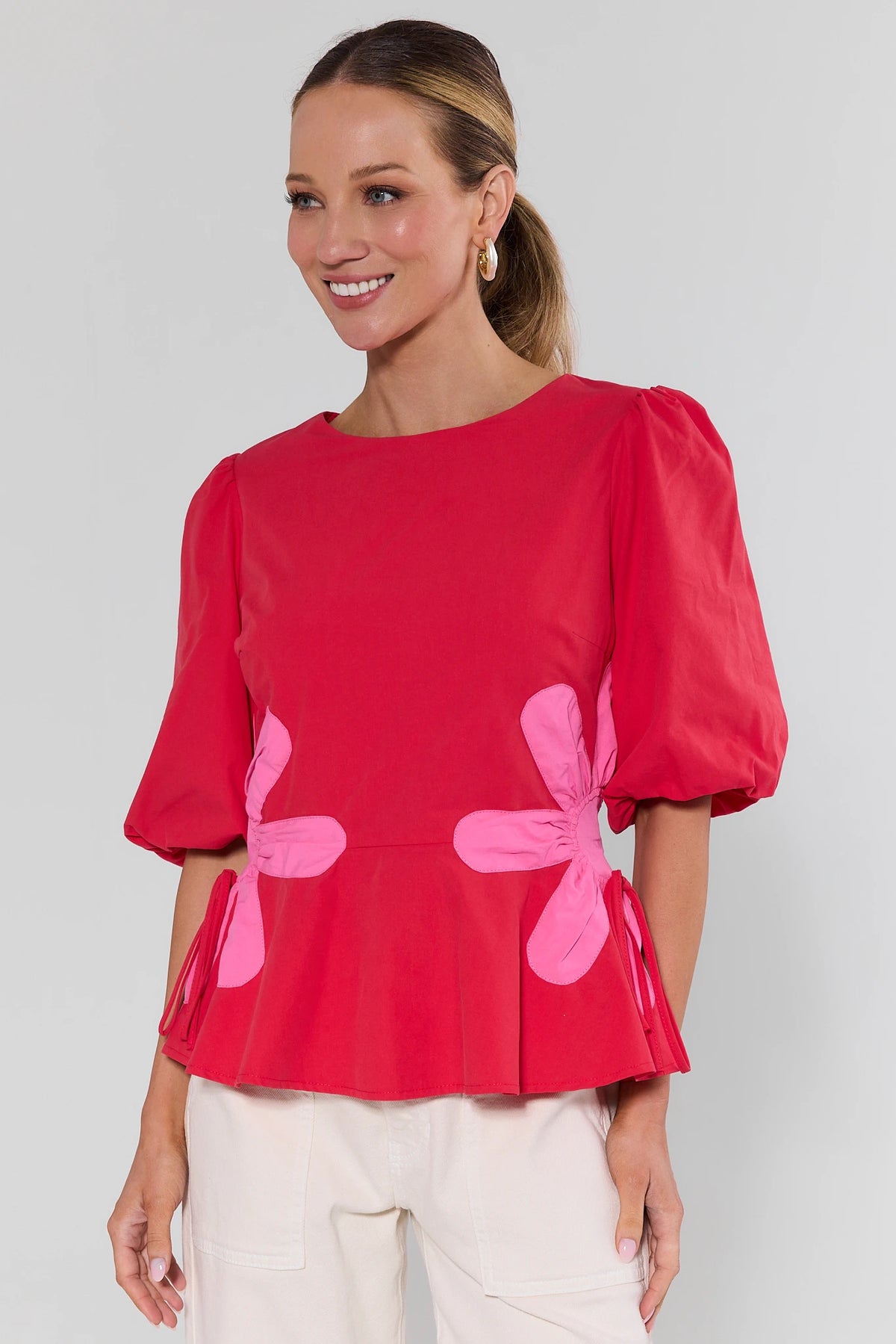 Woman wearing a red blouse with pink floral designs on a plain background