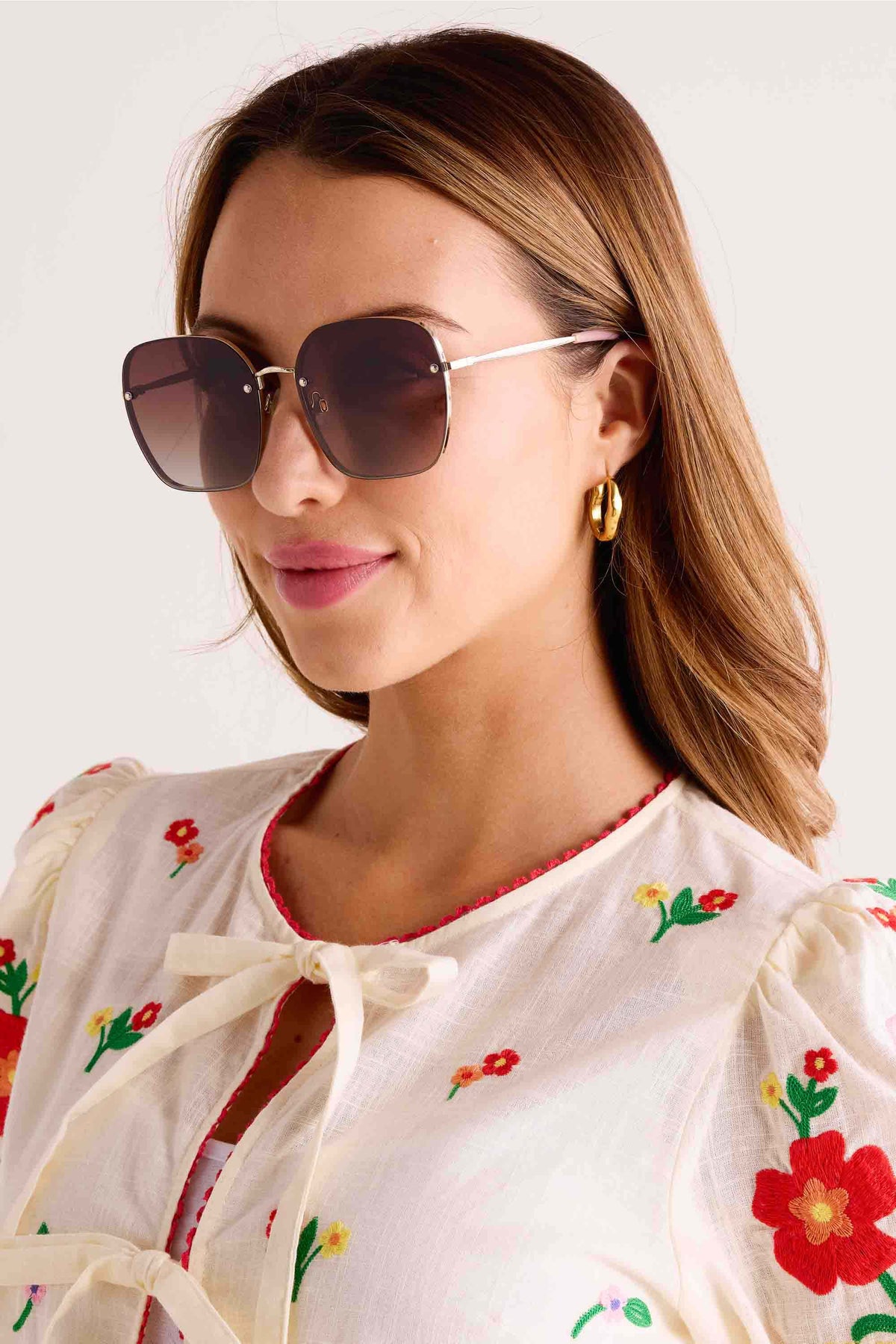Woman wearing Emerson Round Polarized Sunglasses with gradient lenses, thin metal frames, and adjustable nose pads. Styled with chunky gold hoop earrings and floral embroidered top.