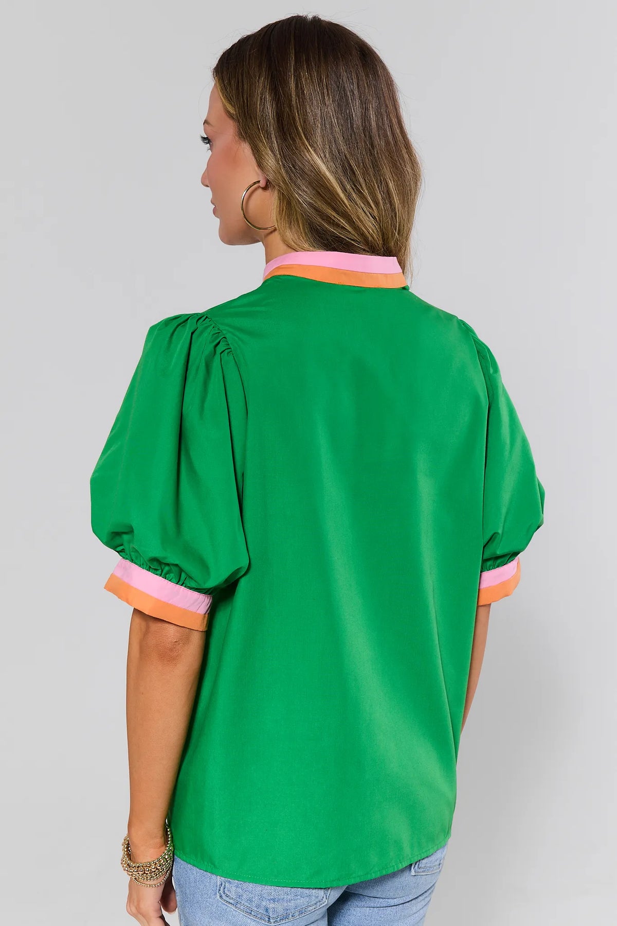 Woman standing wearing a green blouse with colorful cuffs and collar on a plain background