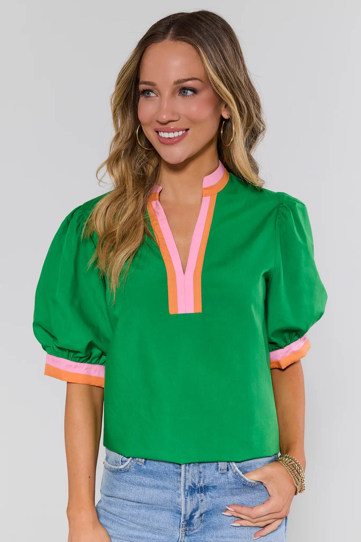 main Woman wearing a green blouse with colorful trim on a plain background