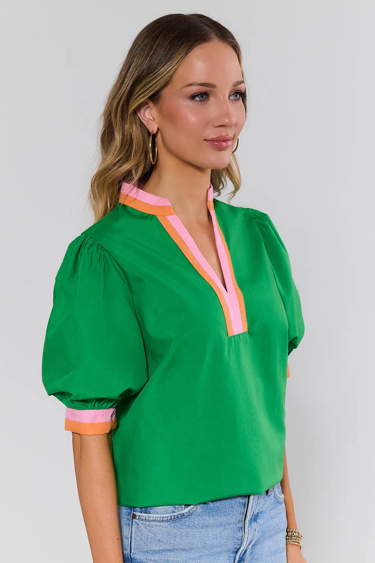 side shot Woman wearing a green blouse with pink accents on a plain background