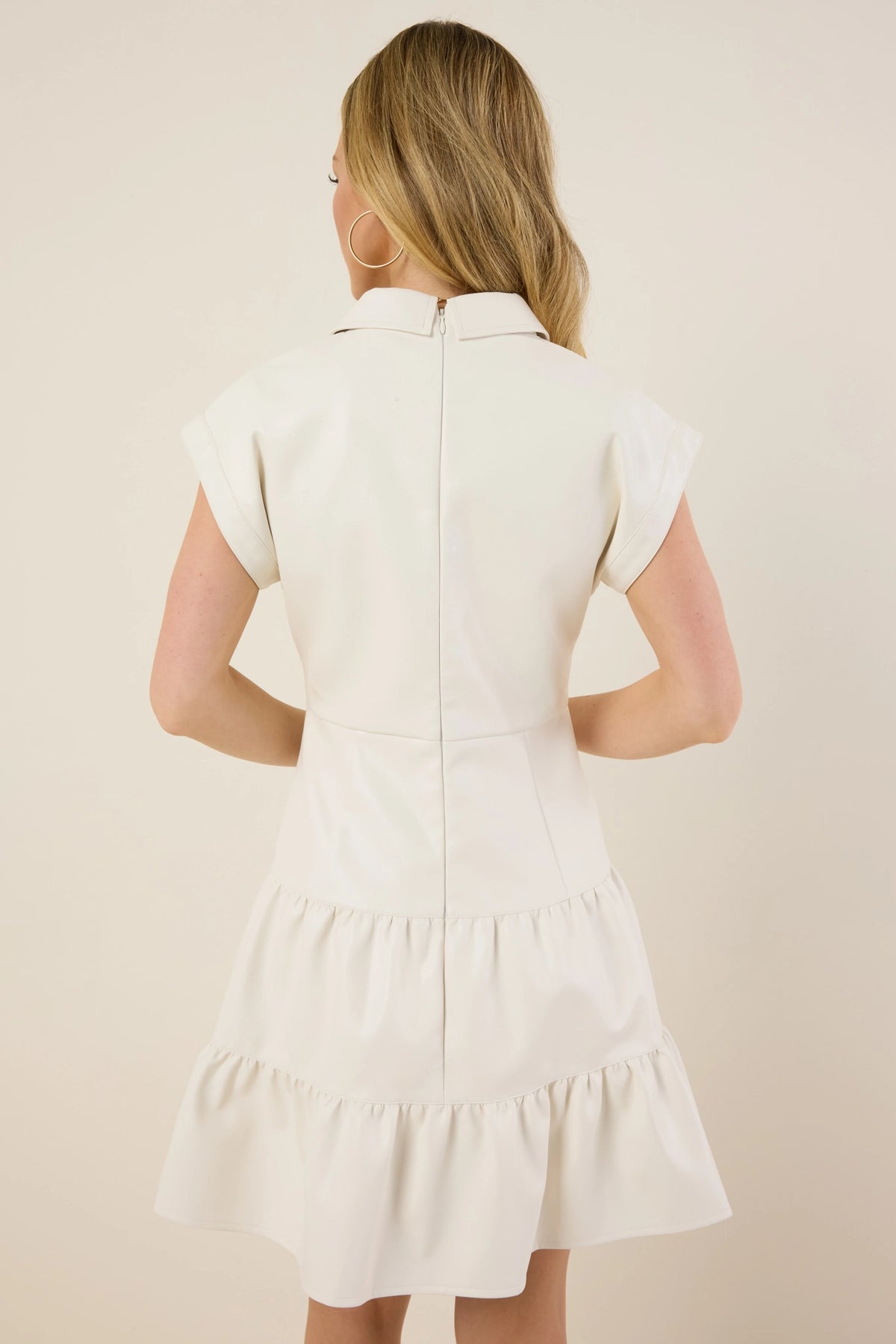 Sawyer Dress: Woman in ivory dress with a small collar, capped sleeves, fitted bodice, and two-tiered ruffled skirt, showcasing a modern faux leather design.
