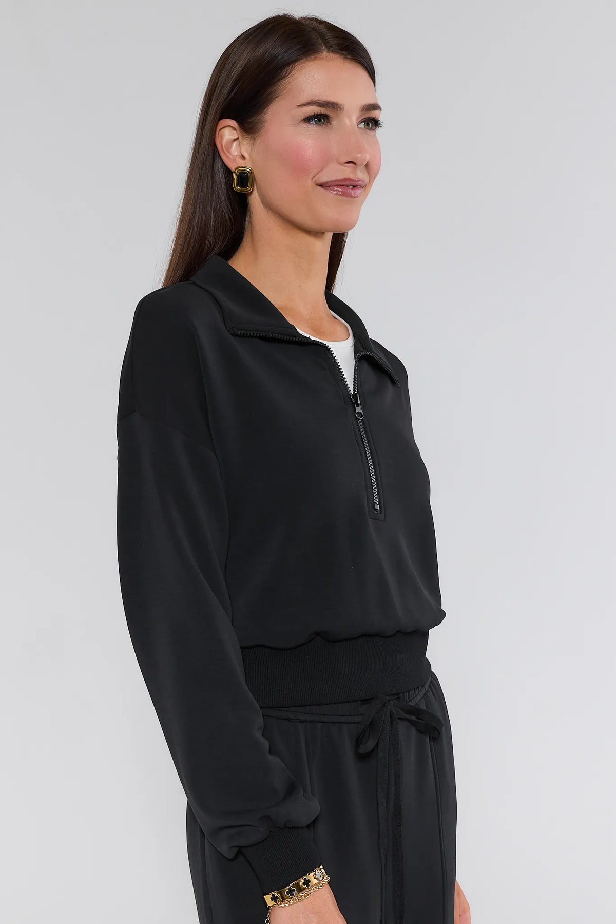 Lucy Black Half Zip Pullover side profile view, ribbed cuffs and waistband, matching pants, gold bracelet | Avara