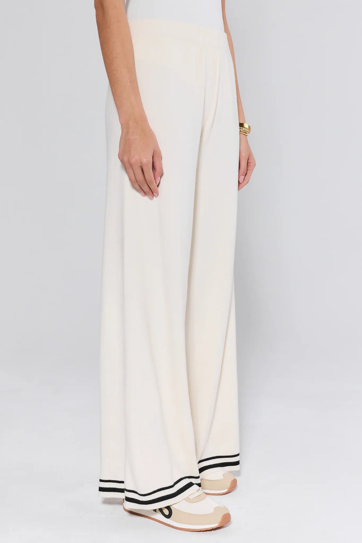 Lexie Ivory Knit Pants side view showing wide-leg fit, elastic waist, and black stripe hem detail with gold bangles - Side Profile | Avara