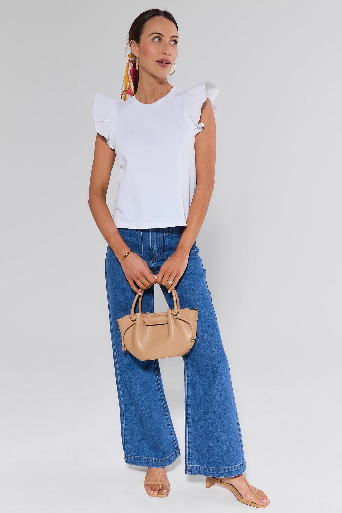 Woman in Rolla's Sailor Flare Jeans, white ruffle top and beige bag - Full Styled Look | Avara