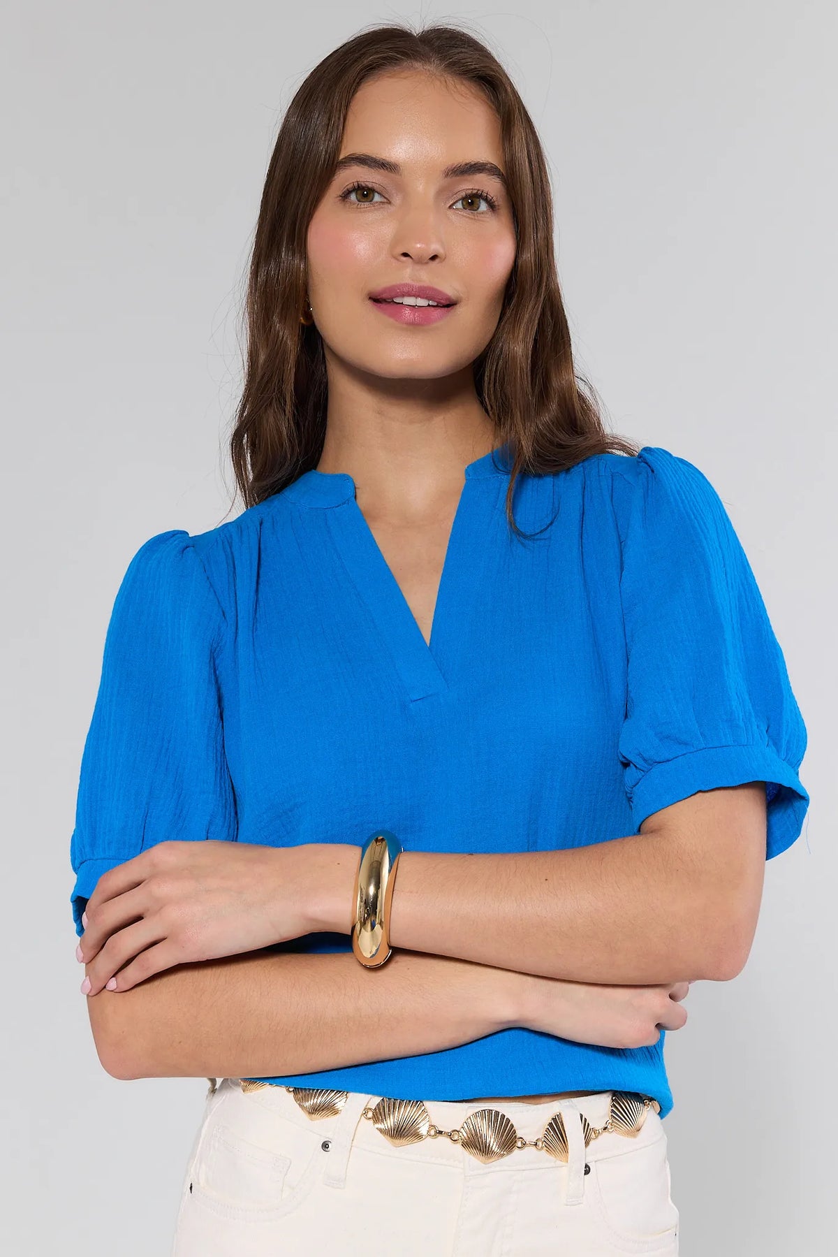 Woman wearing the Marisol Gold Bangle Bracelet, a chunky polished accessory on her right wrist, paired with a cobalt-blue blouse and decorative gold chain belt.
