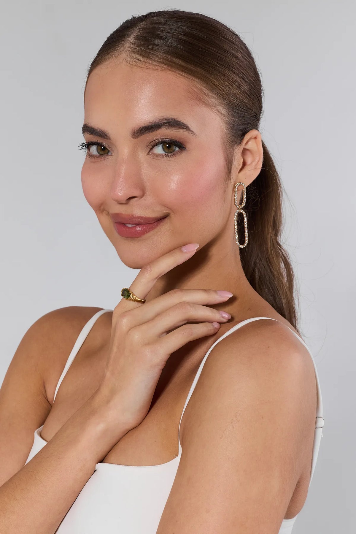 Young woman showcasing the Verna Green Stone Ring, featuring 18k gold-plated hardware and a green gemstone, complemented by linked-oval drop earrings.