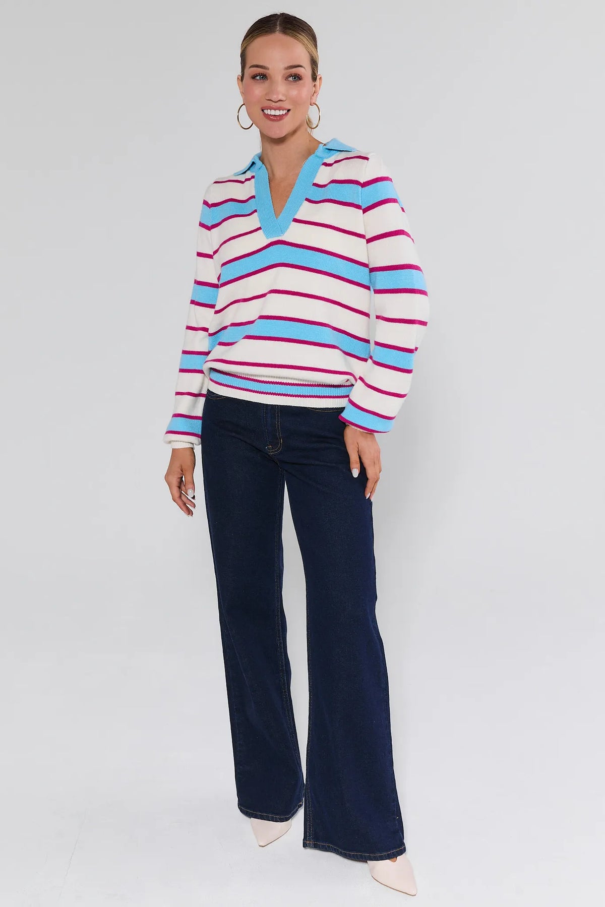 Woman wearing a colorful striped sweater and dark jeans on a white background