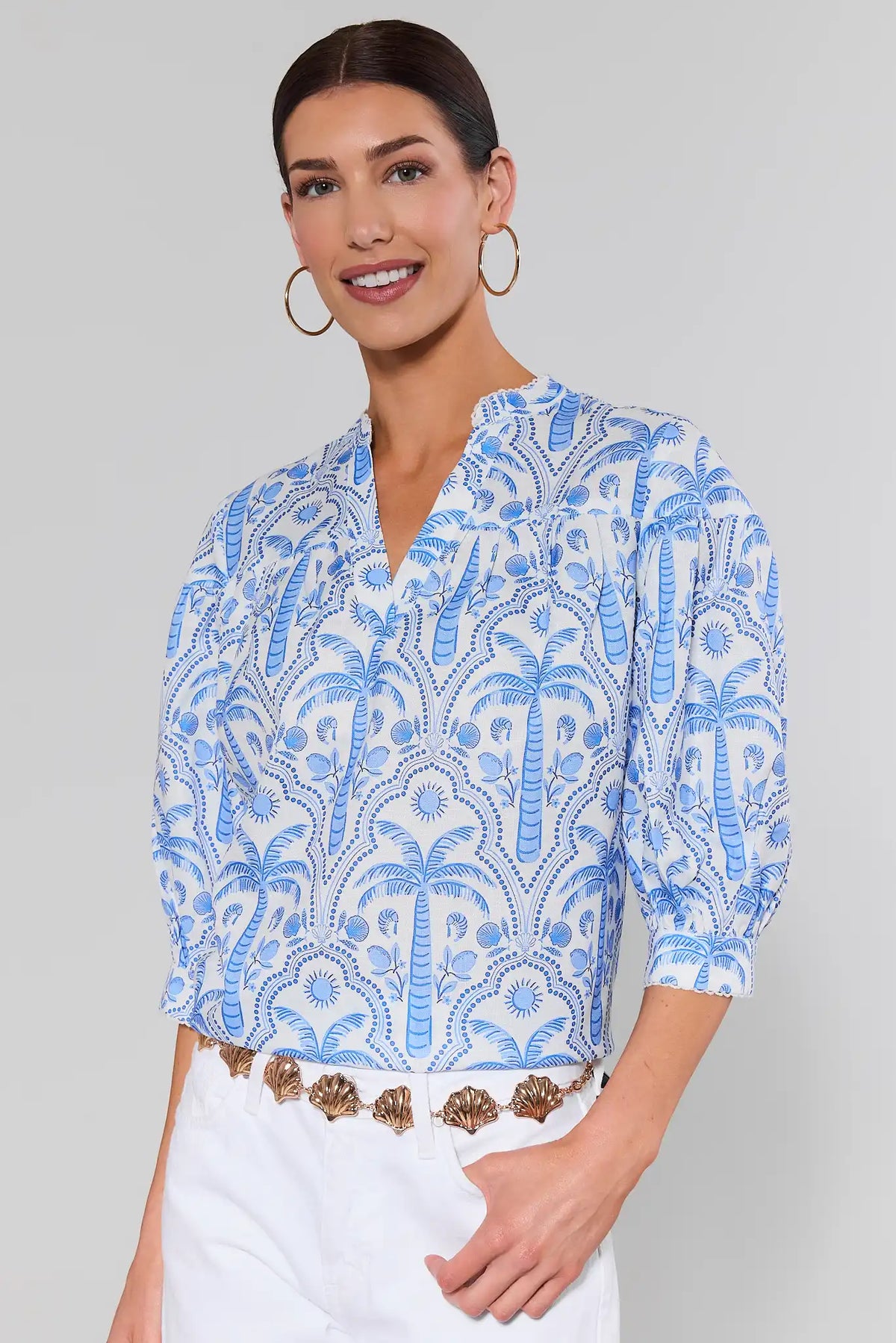 Woman wearing a blue patterned blouse and shell belt with a plain background