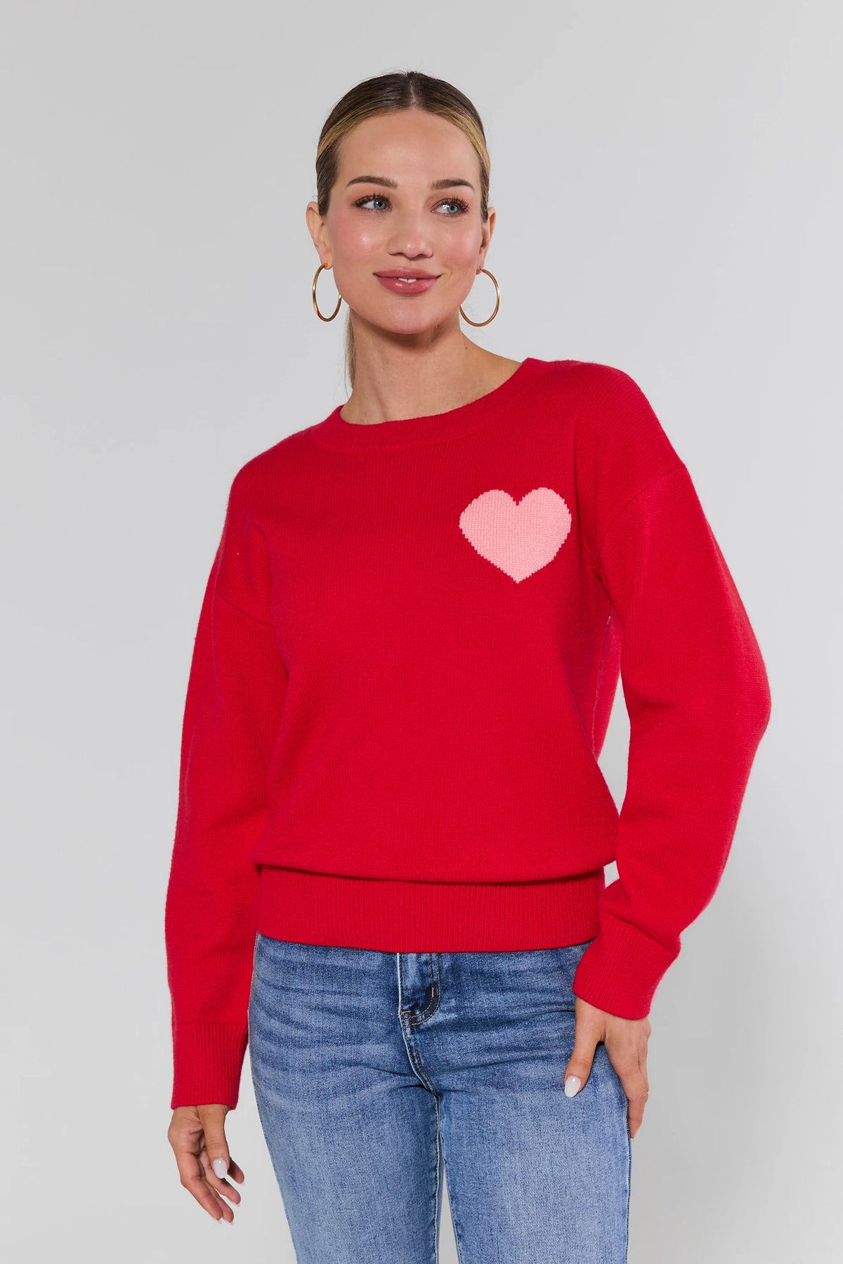 Woman wearing a red sweater with a pink heart design on a plain background