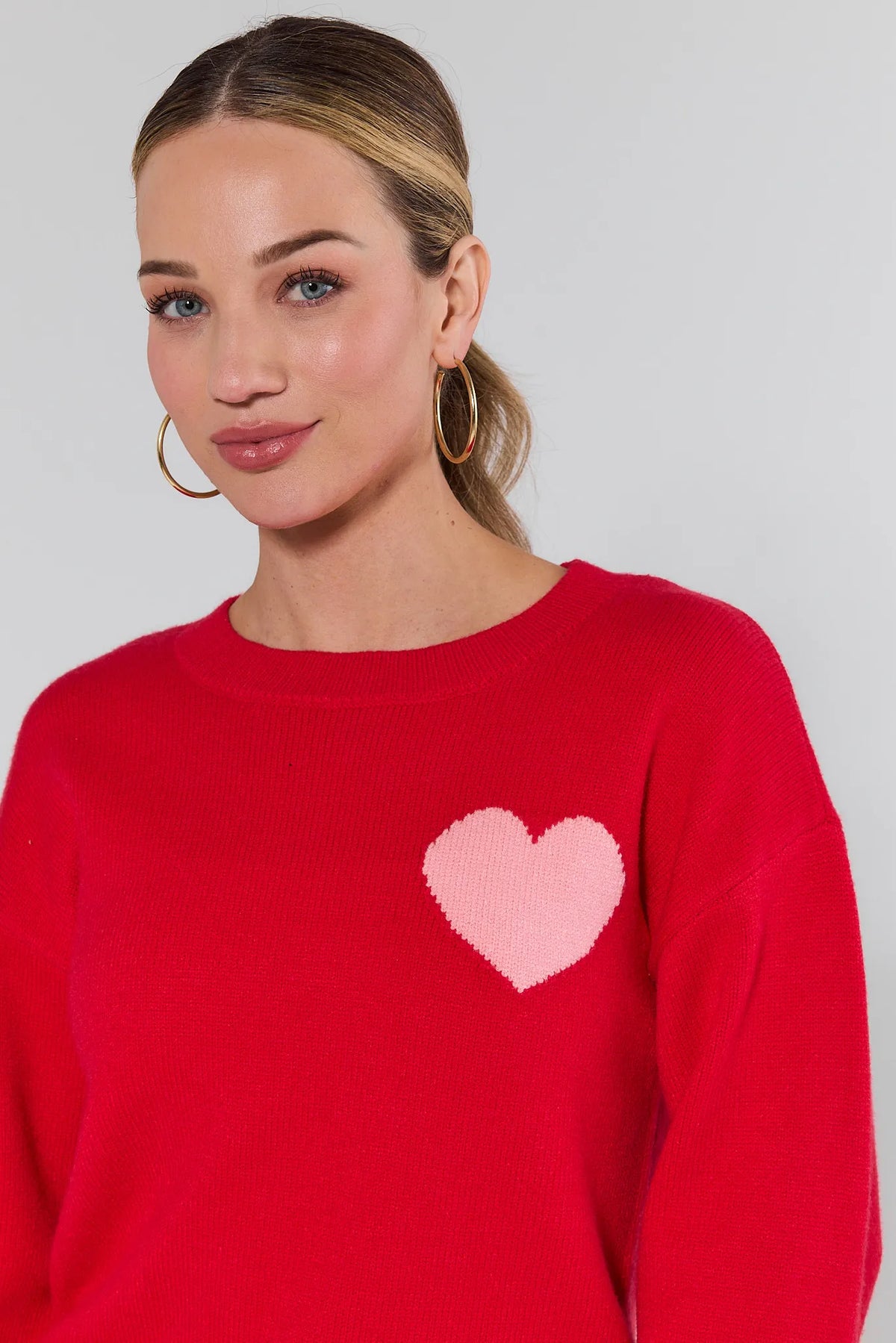 Woman wearing a red sweater with a pink heart design on a plain background