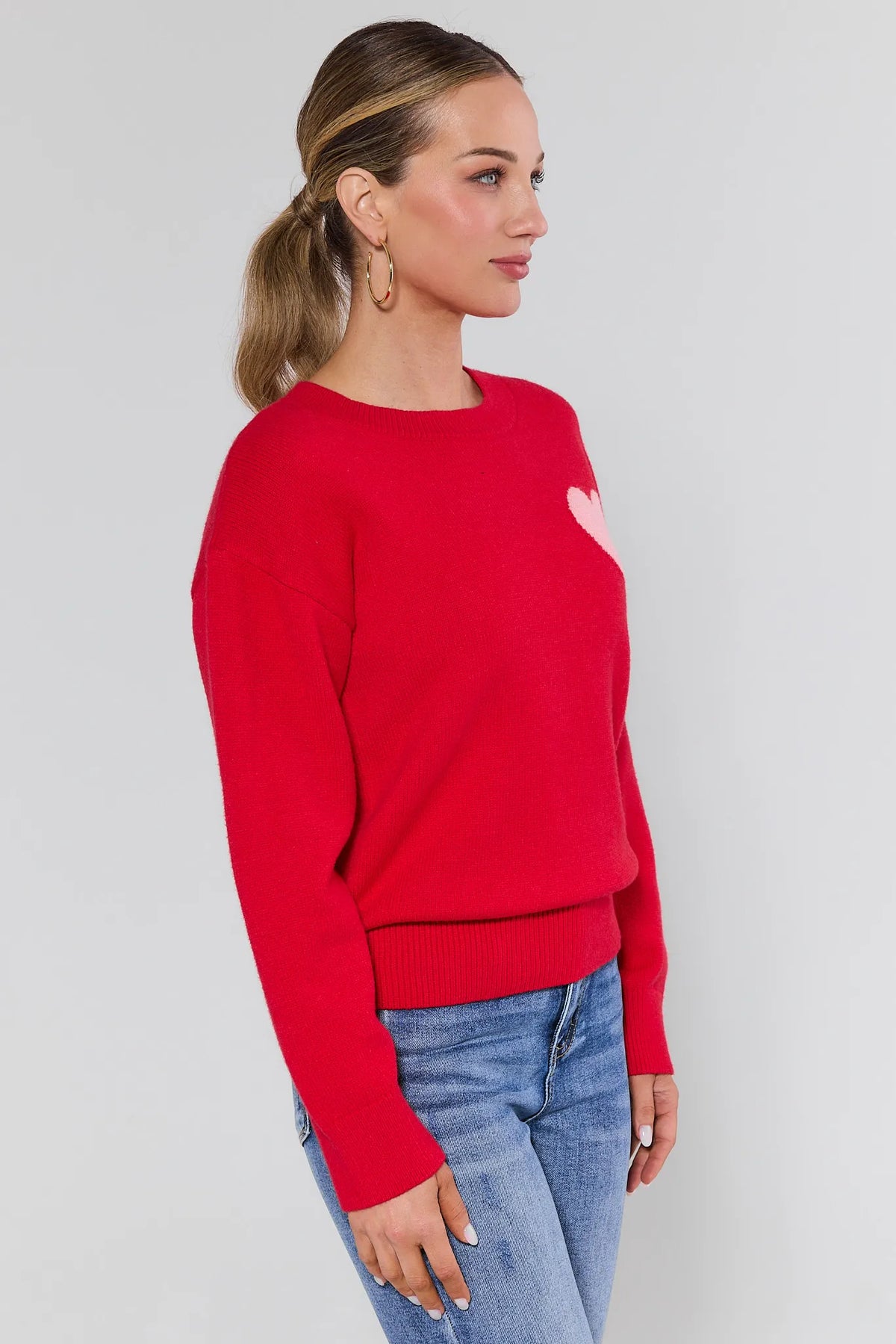 Woman wearing a red sweater with a heart design on a plain background