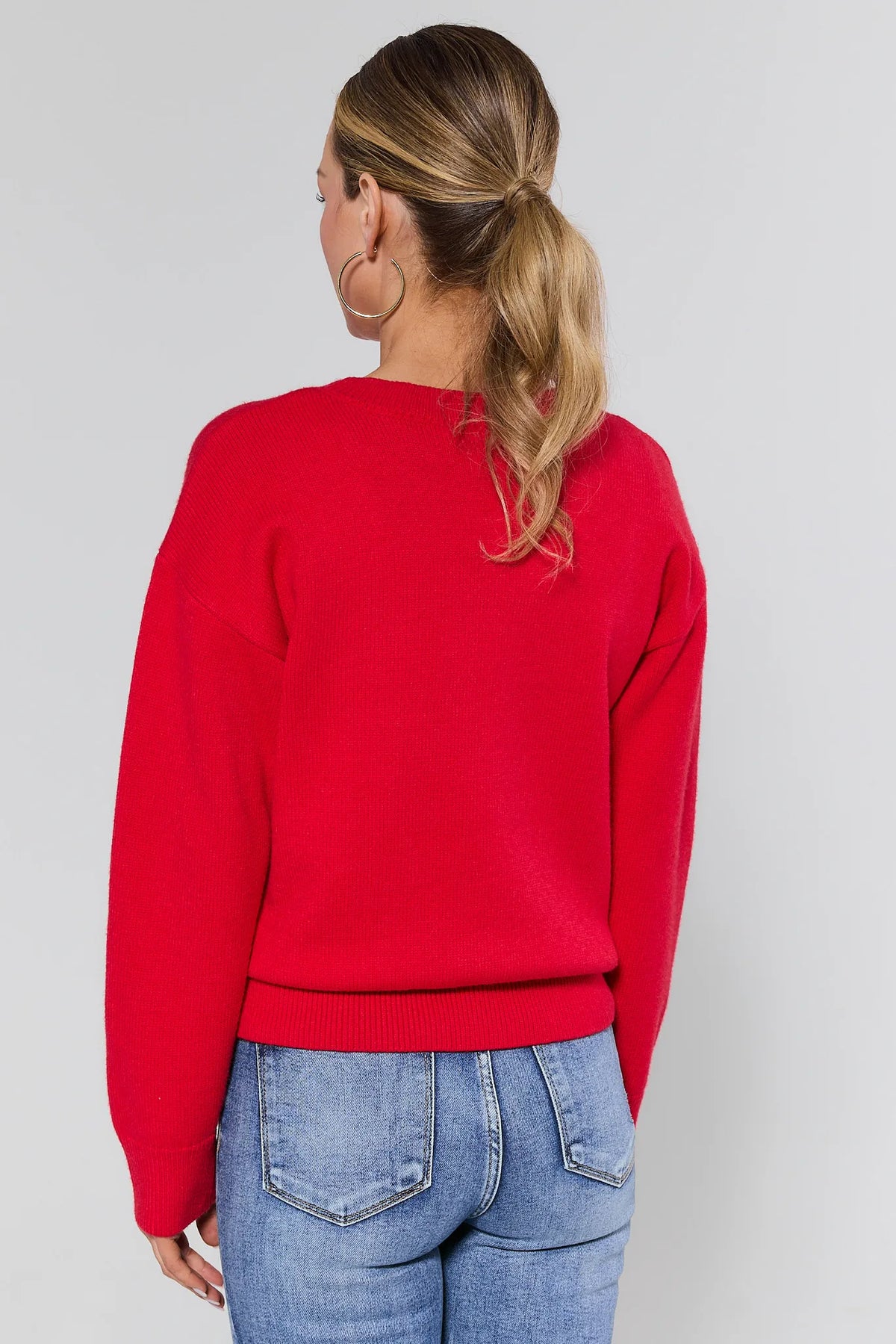 Person wearing a red sweater and blue jeans on a plain background