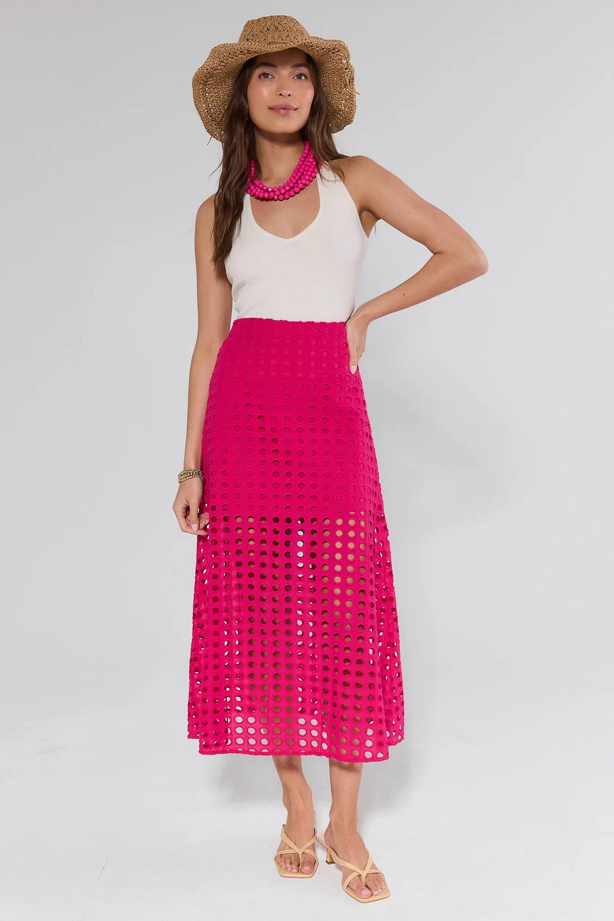 Model wearing Ellie Pink Eyelet Midi Skirt, featuring a high-waisted, ankle-length design with circular cutouts, paired with a tank top, sun hat, and sandals.