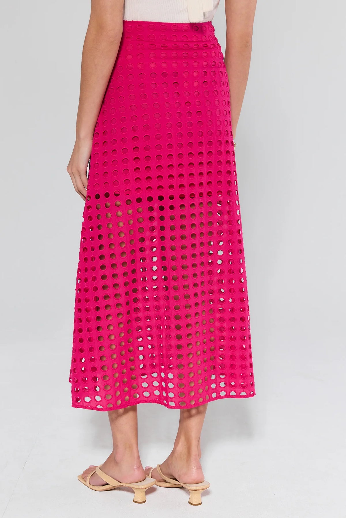 Person wearing the Ellie Pink Eyelet Midi Skirt, showcasing its A-line silhouette, allover eyelet embroidery, and banded waist in a studio setting.