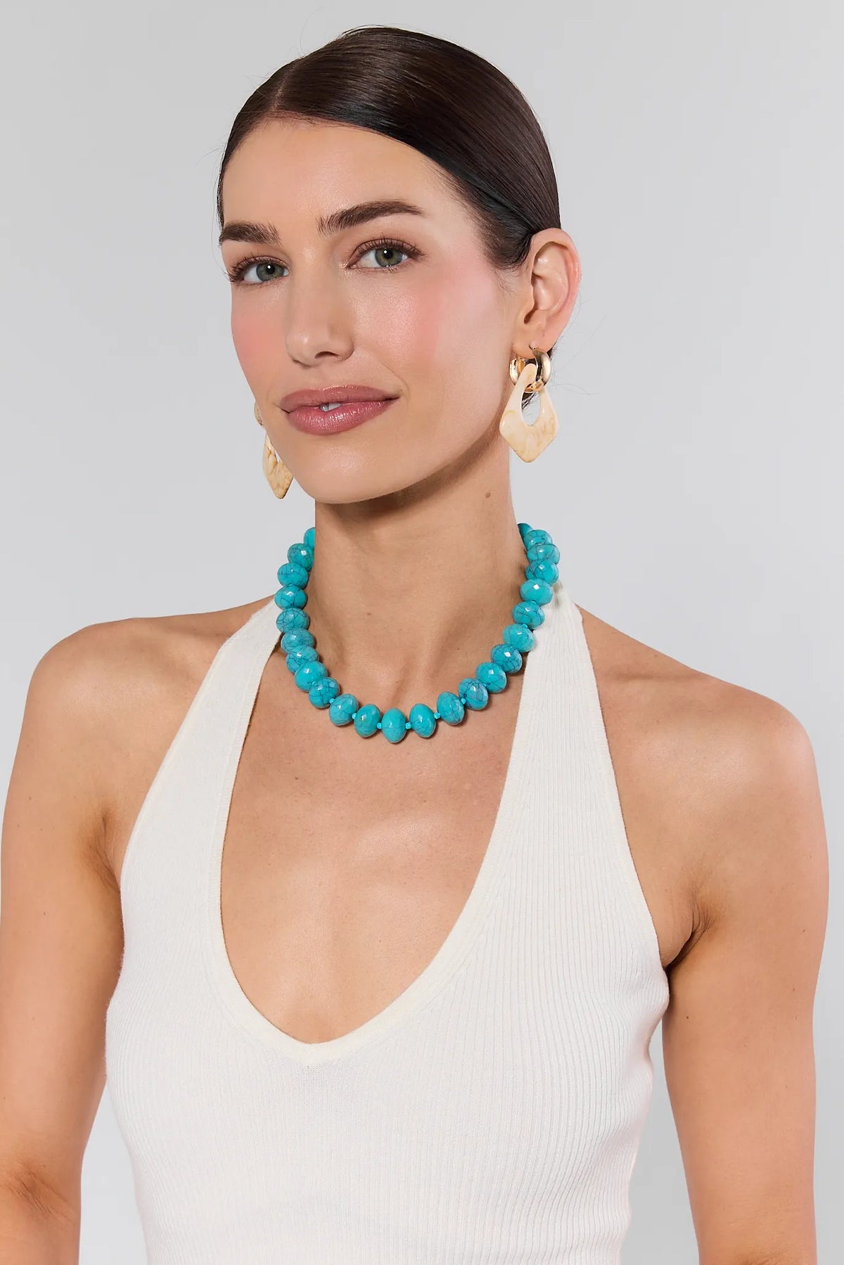 Woman wearing turquoise beaded necklace with gold earrings and white halter top, on-model front view | Avara