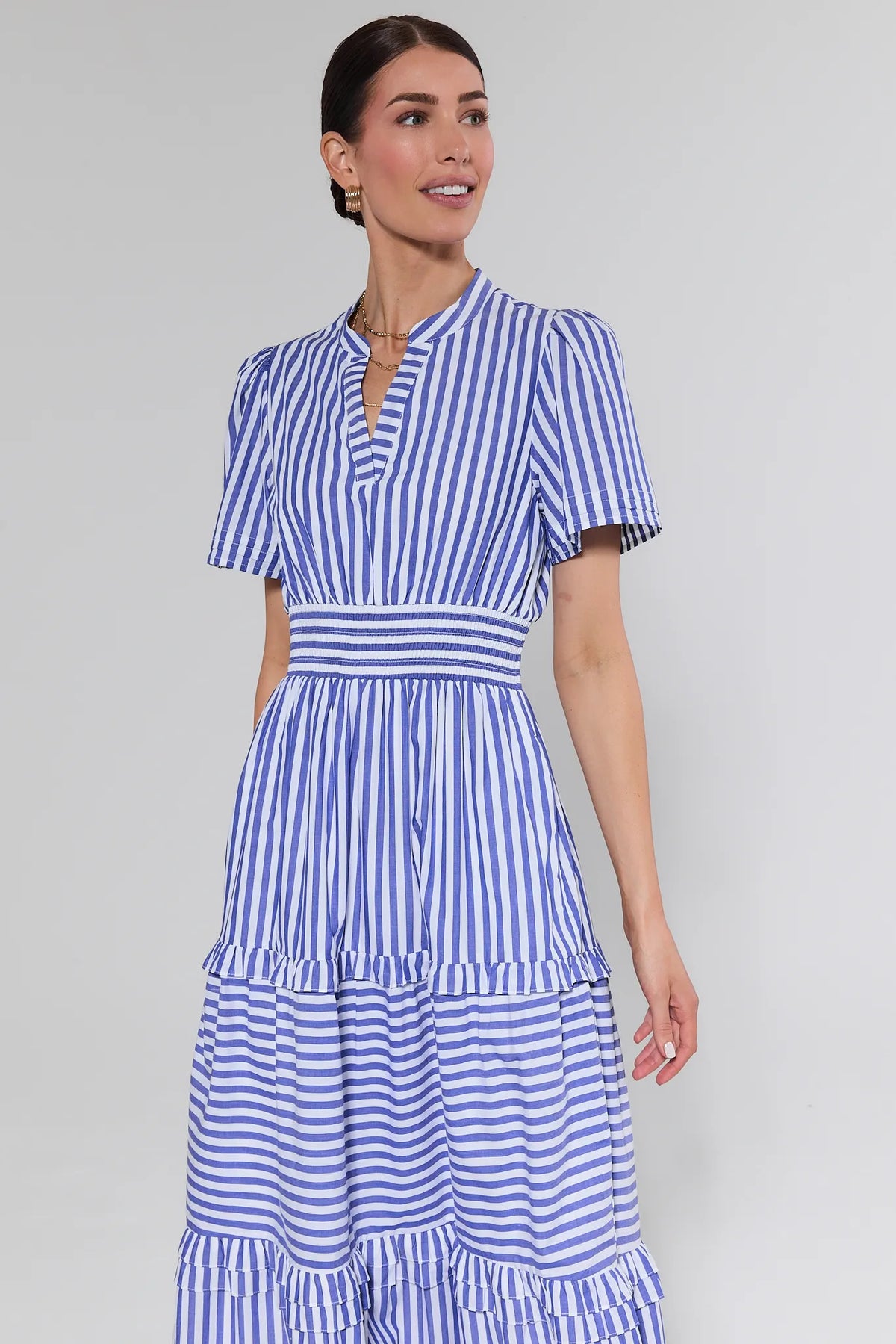 Woman wearing Bella Blue Striped Maxi Dress with short sleeves, V-neck, smocked waist, tiered skirt. Simple accessories include hoop earrings and a necklace.