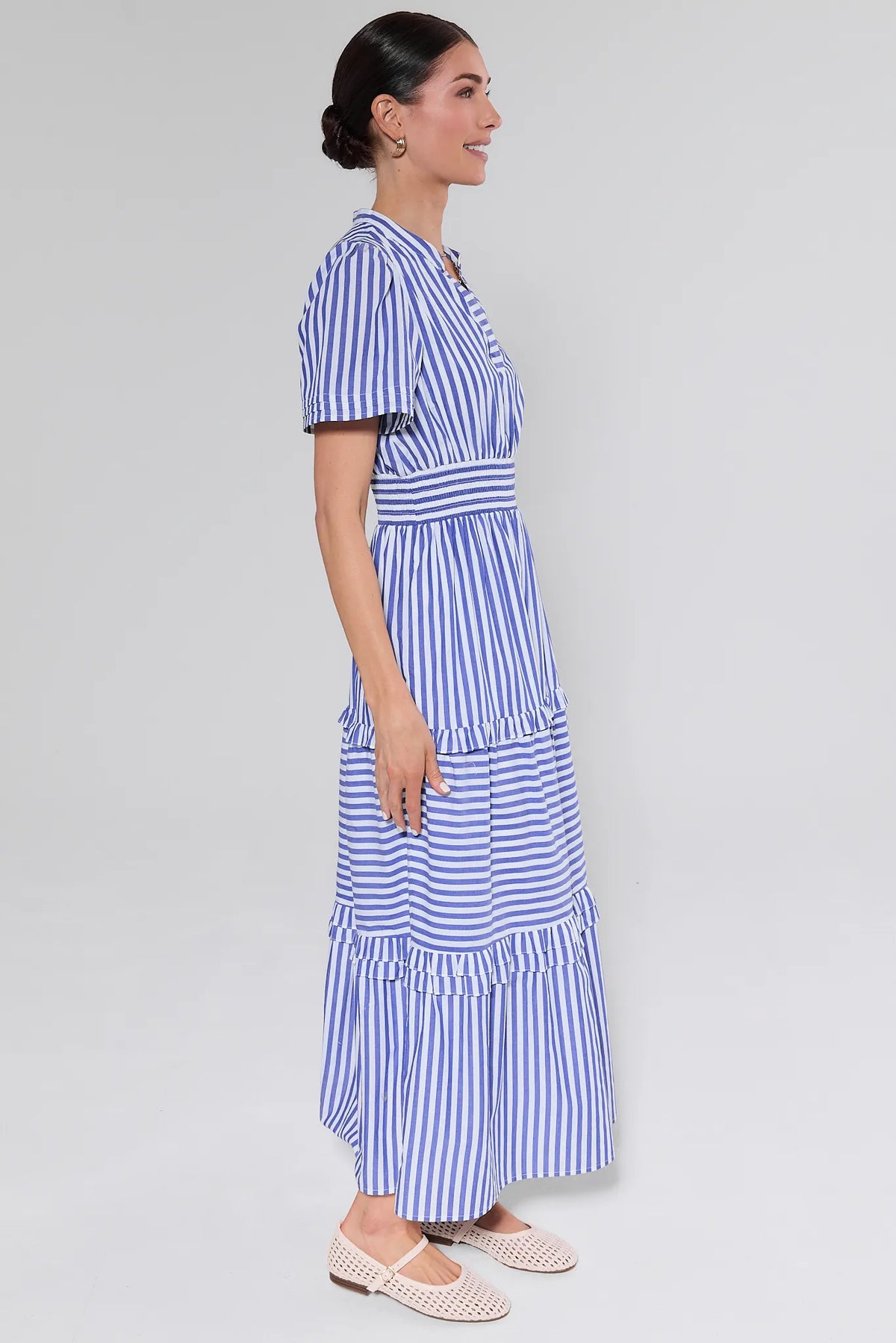 Woman in profile wearing the Bella Blue Striped Maxi Dress with tiered ruffles, short sleeves, and smocked waistband, paired with light-colored flats.