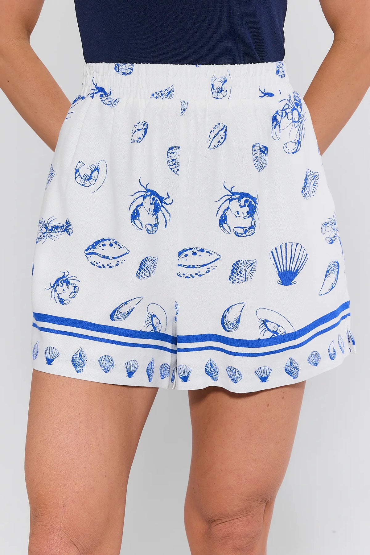 White seashell print shorts with blue shell pattern and elastic waist, close-up front view | Avara