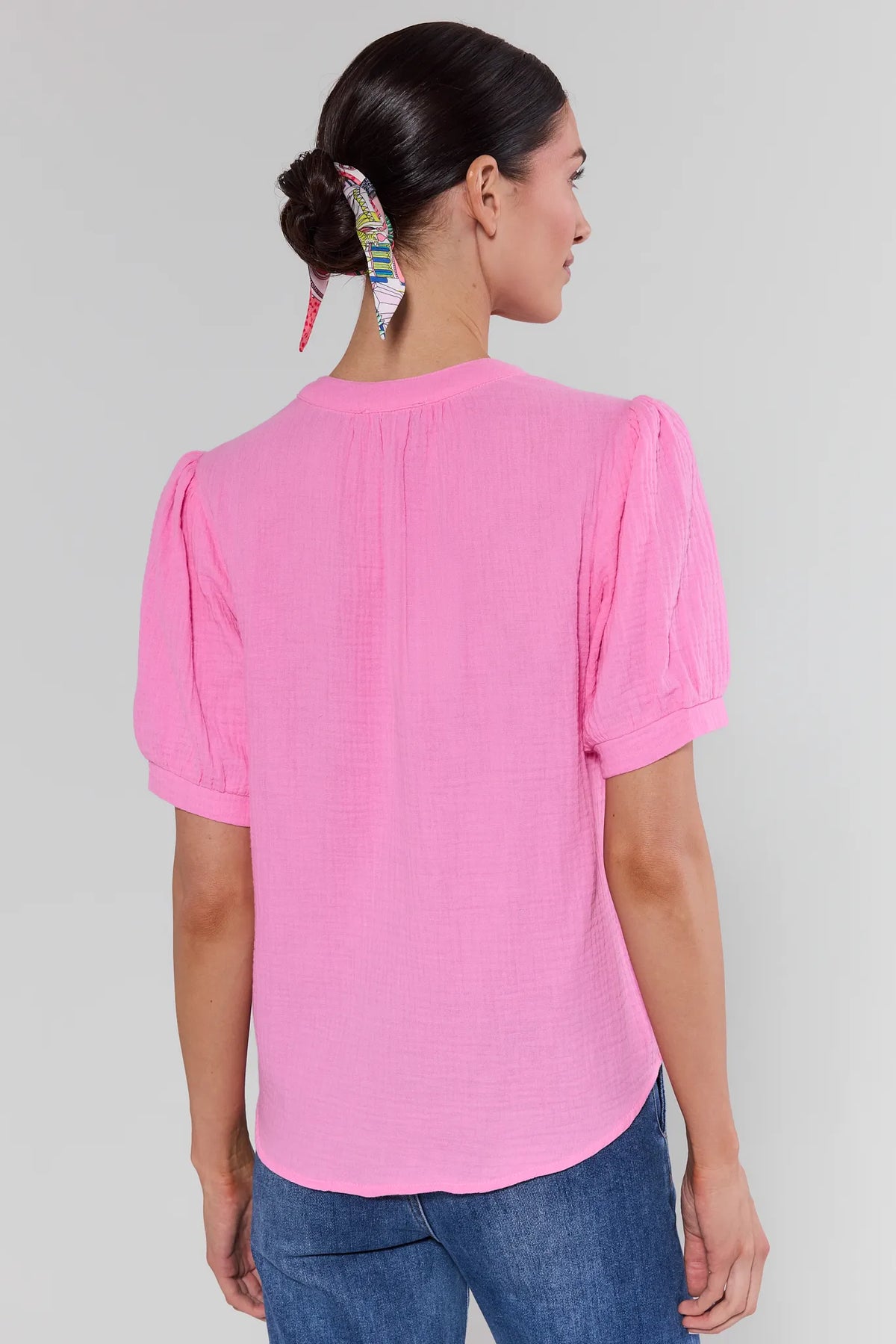 Woman wearing a pink blouse with short sleeves and blue jeans on a plain background