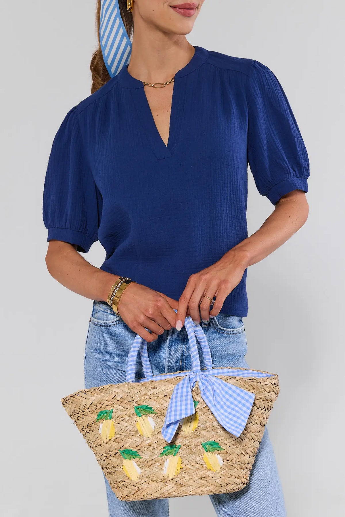 Woman holding lemon raffia straw tote bag with blue gingham bow, styled with navy top and jeans | Avara