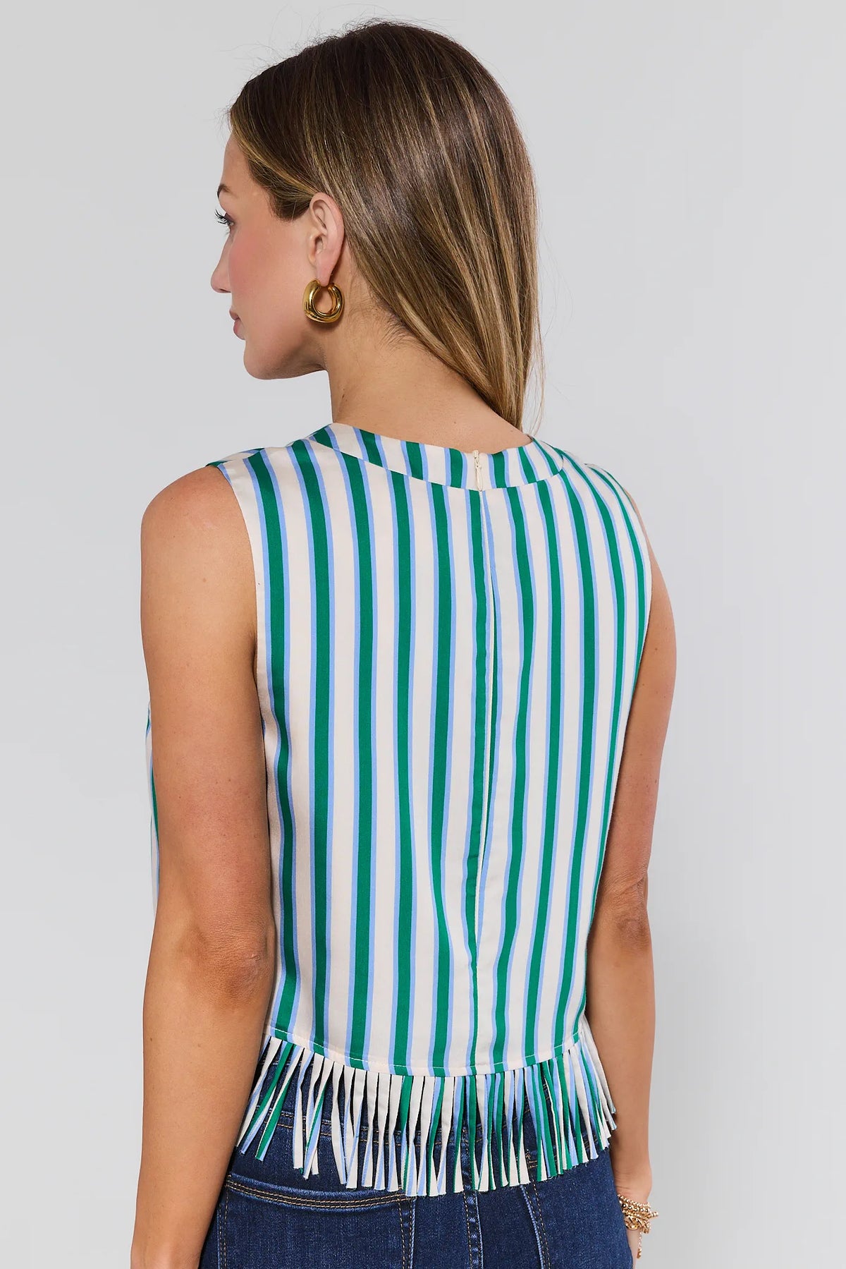 Woman wearing a green and white striped sleeveless top with fringe details on a plain background