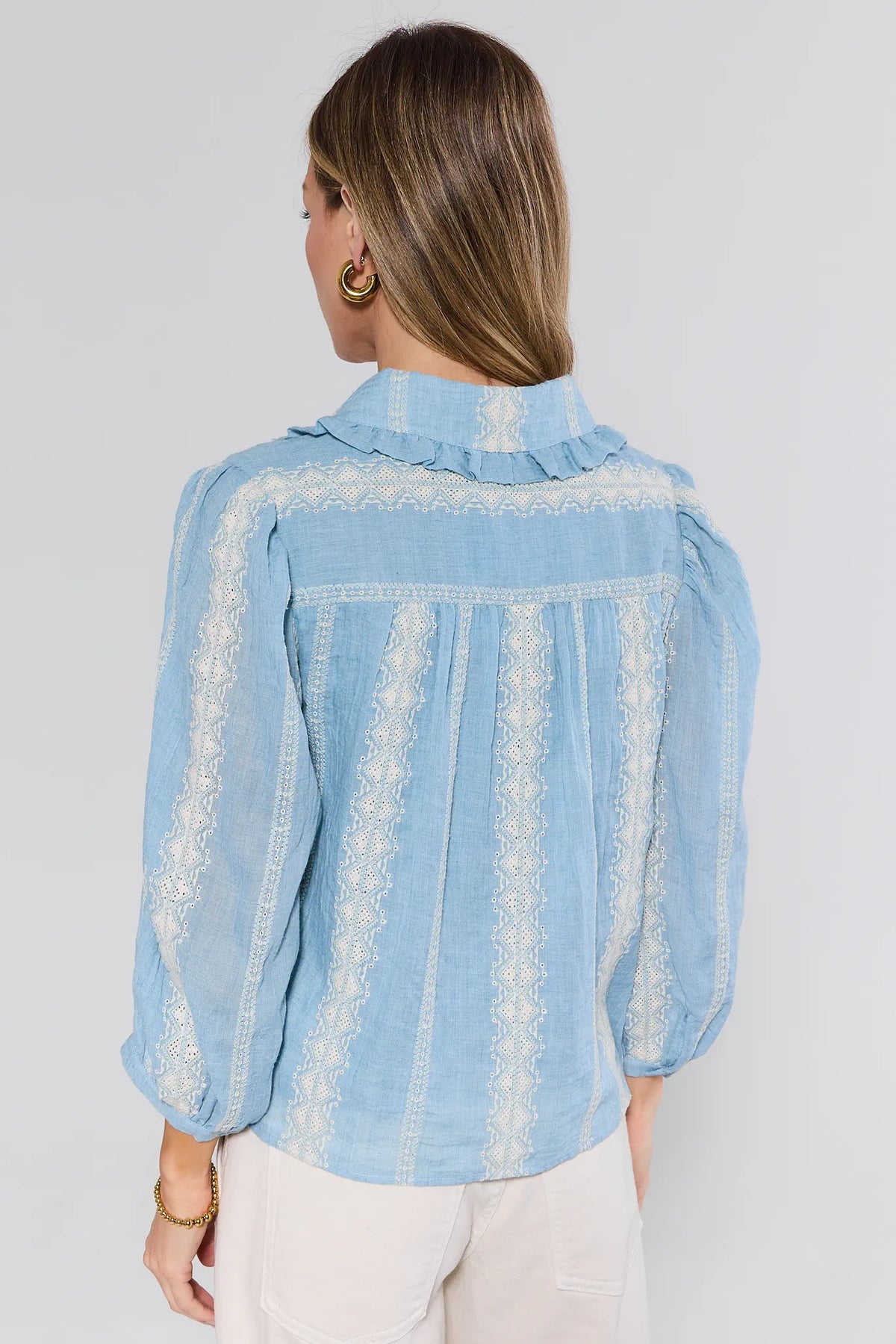 Woman wearing a light blue denim shirt with lace details on a plain background