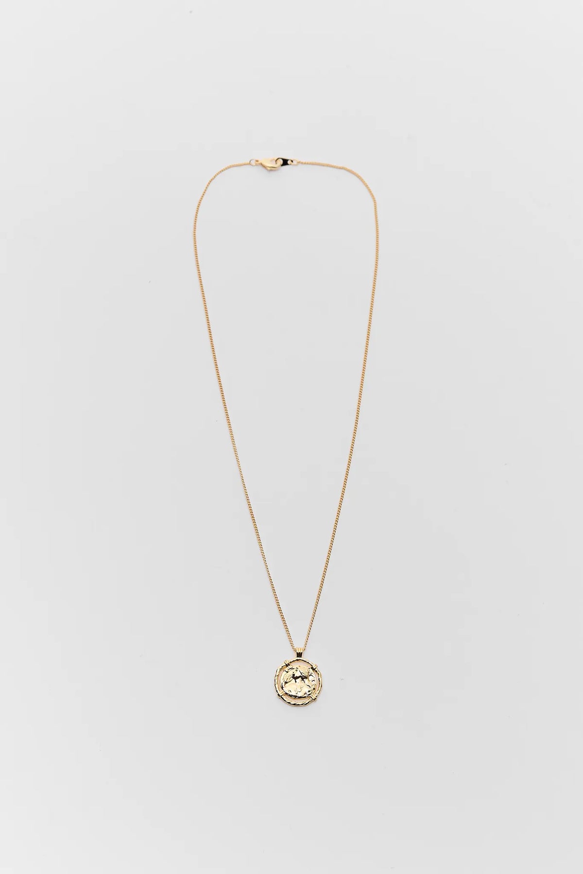 Gold necklace with a circular pendant on a light gray background