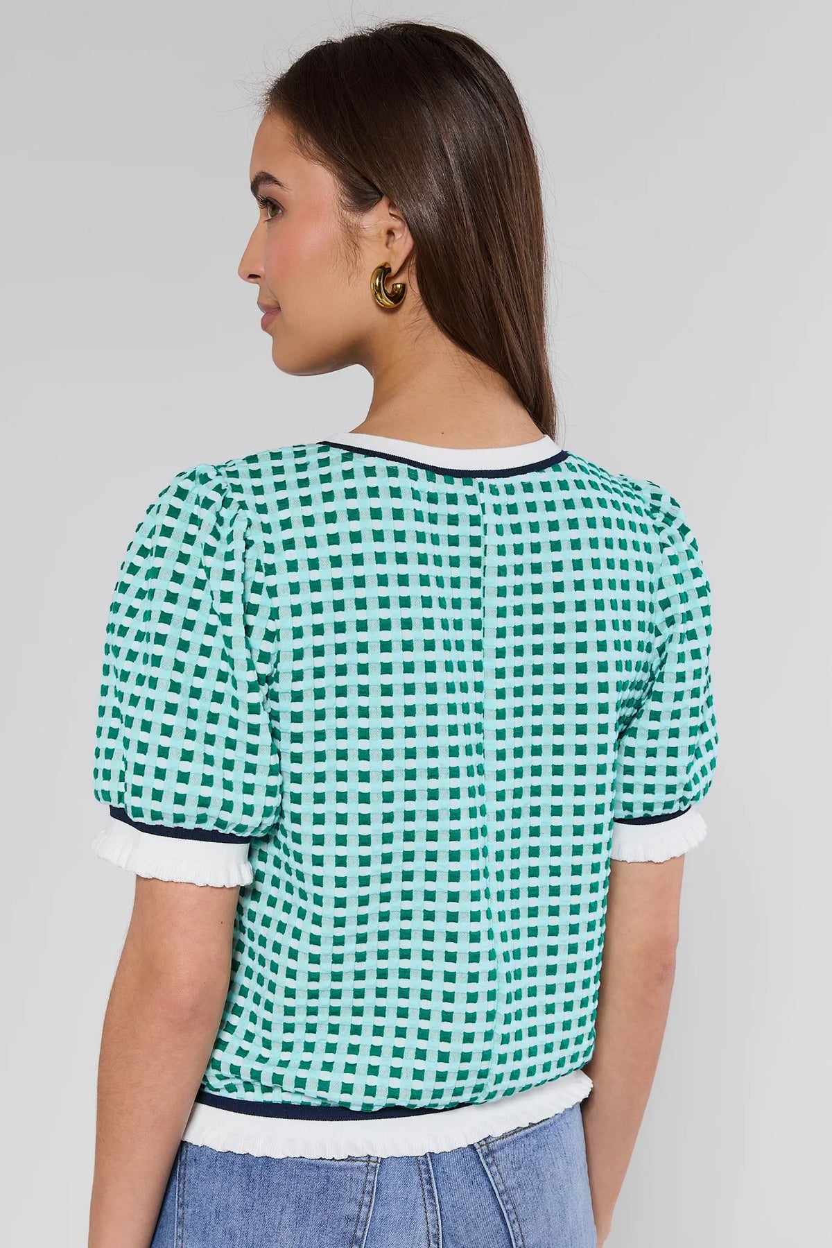 Woman wearing a green and white checkered blouse with blue jeans on a plain background