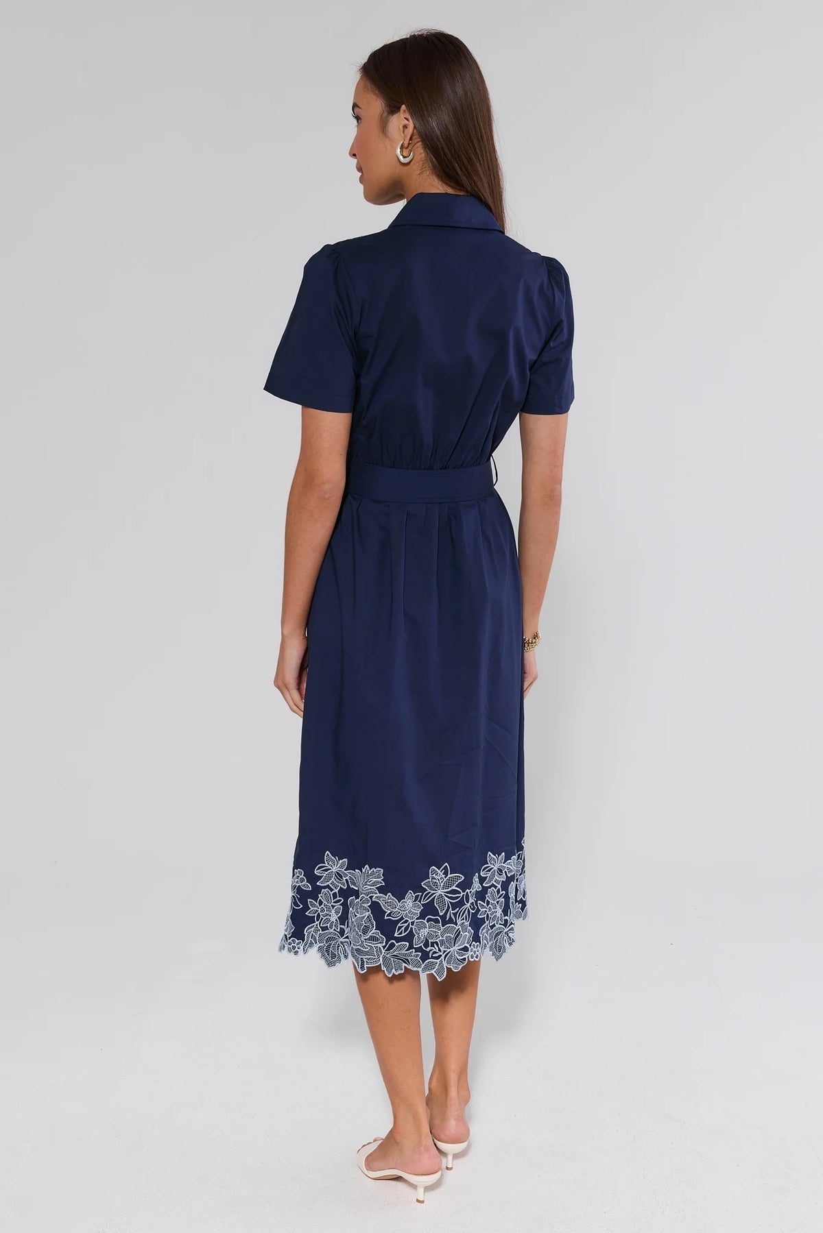 Navy blue midi dress with white floral embroidery at hem, scalloped lace border, back view on model | Avara