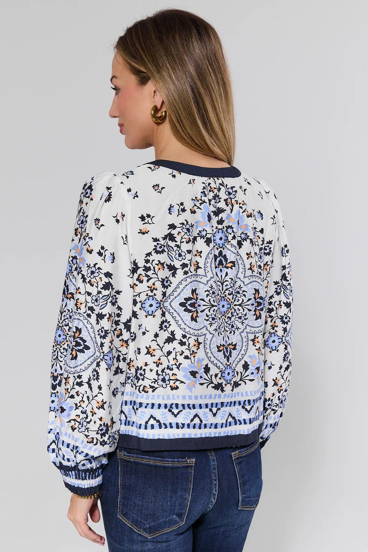 Woman wearing a patterned blouse and jeans on a plain background
