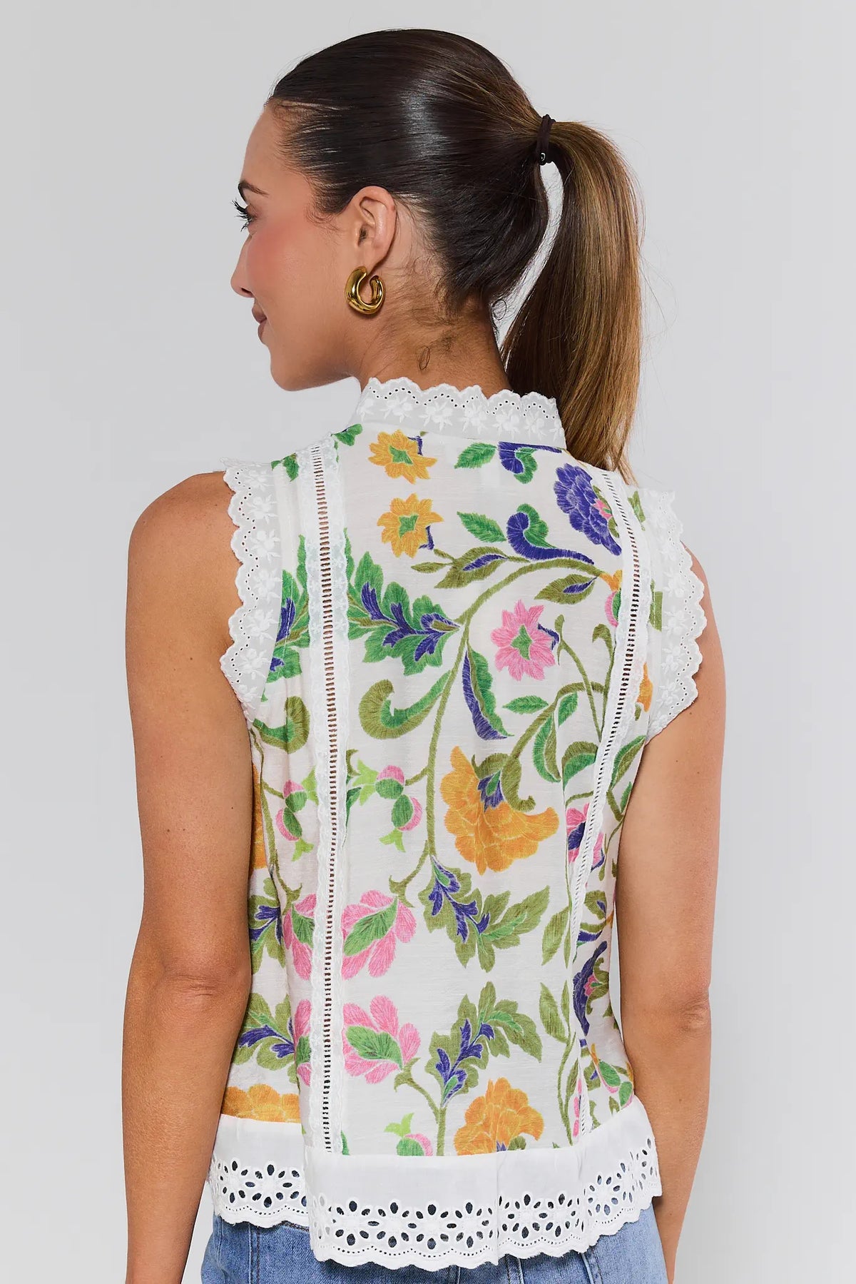 Woman wearing a sleeveless top with floral embroidery on a plain background